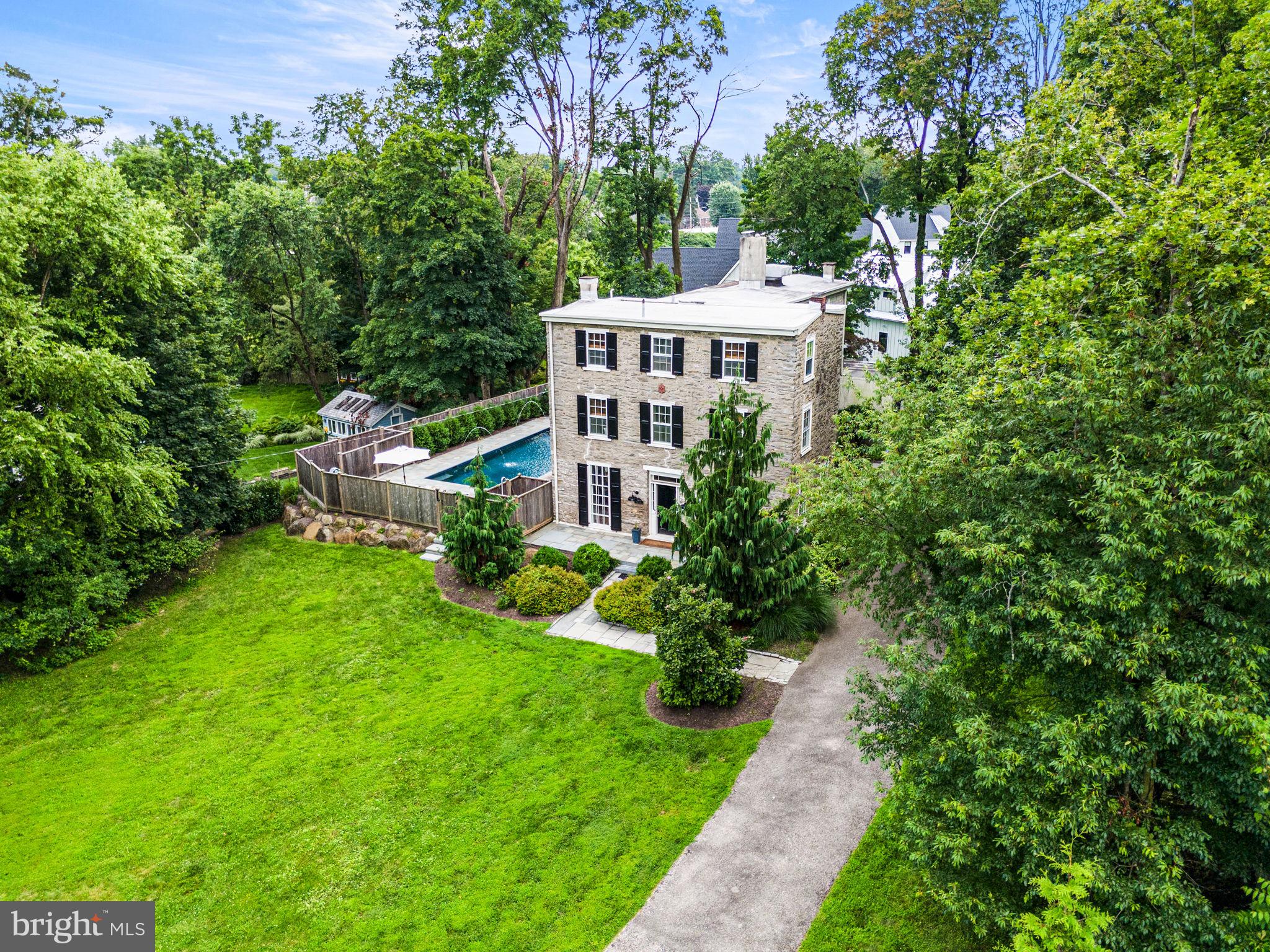 Tucked away on a quiet cul-de-sac in Wyndmoor, this picturesque Federal-style residence—originally built in 1810—has been thoughtfully expanded and upgraded, showcasing classic architecture reimagined for today’s lifestyle. A private drive leads to a slate walkway and entry, setting the tone for the home’s timeless appeal. Inside, rich architectural details abound, including random-width hardwood floors, deep-set windows, hand-carved fireplace mantels, and floor-to-ceiling windows that flood the interiors with natural light. Just off the center hall, a graceful archway leads into the living room with a gas fireplace, while the adjacent dining room features another gas fireplace with an intricately carved mantel and floor-to-ceiling French doors that open to the sunroom. The kitchen is both functional and refined, offering granite countertops and backsplash, a breakfast bar, Viking range, Sub-Zero refrigerator, a side entry, secondary staircase and doors to the laundry room, which provides access to the two-car garage. The expansive sunroom—framed by walls of windows—overlooks the flagstone terrace, pool, and outdoor fireplace, creating seamless indoor-outdoor living. A newly renovated mudroom with powder room and a spacious study with built-ins complete the first floor. Upstairs, the primary suite is a true retreat, featuring a sitting room, radiant heated floors, a walk-in closet with custom built-ins, and a luxurious marble bath with walk-in shower, and soaking tub overlooking the pool. A second en-suite bedroom and a guest bedroom complete the second floor. The third level offers two additional bedrooms and a full hall bath. At the rear of the home are utility areas, attic access, and a large bonus room with a full bath, currently used for storage. The professionally designed outdoor spaces include a saltwater pool with fountains, built-in stone fireplace, and an outdoor kitchen complete with a Napoleon grill, sink, beverage fridge, and stone bar—all surrounded by mature landscaping and trees. Just minutes from Chestnut Hill and Wyndmoor's shops and dining, and a short walk to the Benezet train station for easy access to Center City, this exceptional property offers a peaceful retreat in a prime location.