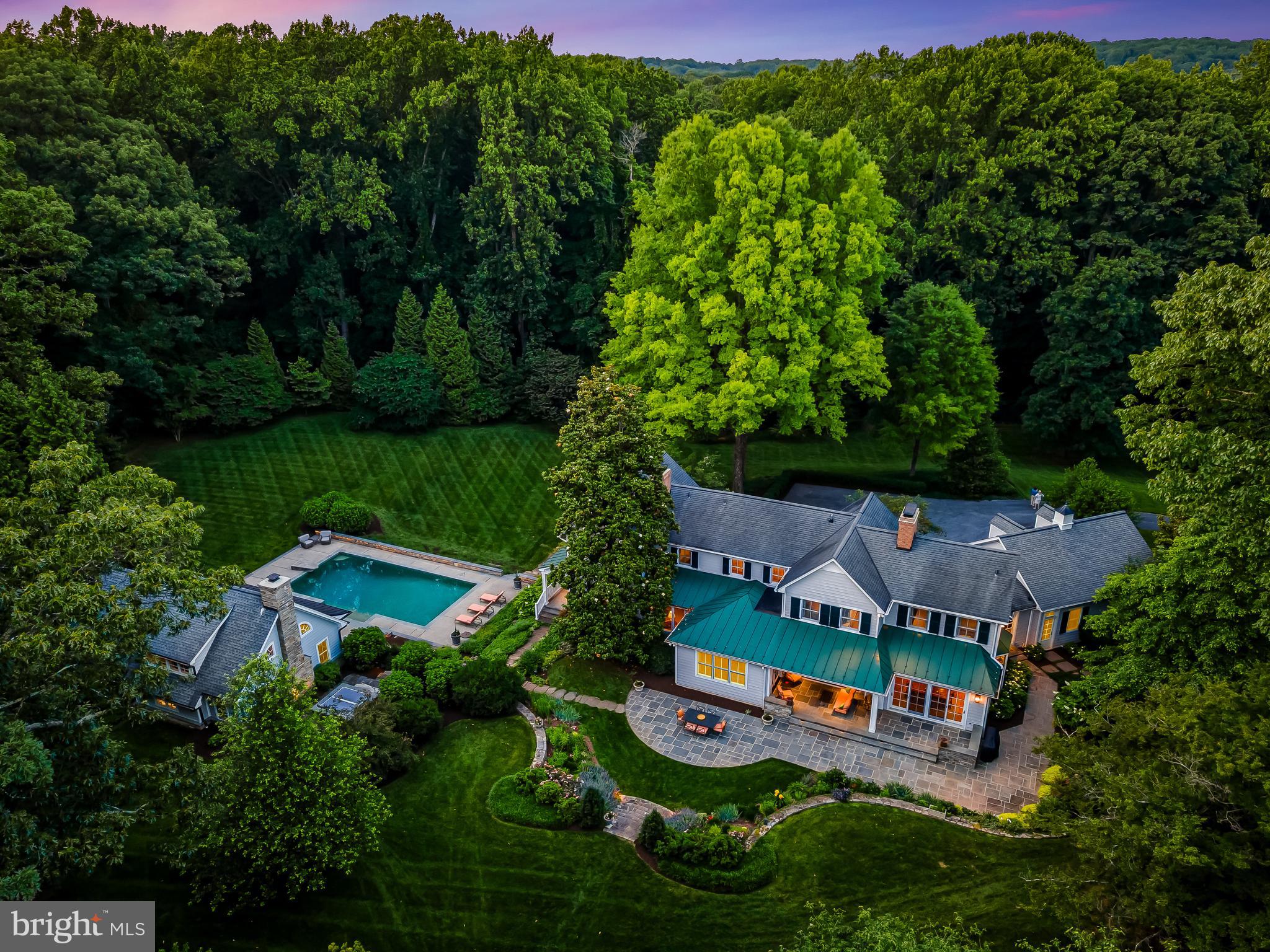 Trust your instincts. Experience unfettered livability and complete privacy on this estate property situated upon 3.5+ acres within a vibrant Greenspring Valley neighborhood. Pass through the neighboring golf course and enter the long private drive to find this remarkably stylish, totally renovated and expanded colonial together with the extraordinary pool house beckoning you to escape to personal retreat and opportunity for grand celebration. Step back in time 45 years to witness the relocation of the Circa 1900s farmhouse, then fast forward 25 years to envision a new family begin a series of masterful renovation and expansion projects, now realized. The residence features meticulously crafted architectural elements, millwork, fine finishes, high-end systems, five fireplaces, and a harmonious unity of traditional elegance and contemporary design. Entertain with ease in the stunning formal living and dining rooms, and casual spaces filled with natural light. Oversized doors open to the surrounding gardens, covered porches, and bluestone terrace with sitting walls for seamless flow between indoor and outdoor spaces. The spacious family room with brick herringbone floor, woodburning fireplace and entertainment center opens to the deluxe chef’s kitchen anchored by a large island with breakfast bar and features premium wide plank oak flooring, honed marble counters, pantry, a gas fireplace for seasonal enjoyment, and space for informal dining. Deluxe stainless appliances include a 6-burner gas cooktop, double wall ovens, and warming drawer. Nearby, a mudroom with cubbies and closets serves as a butler’s pantry with second refrigerator, laundry hook-up, and convenient dog wash. A main level bedroom suite offers private getaway for guests and is adjacent to a charming study opening to a covered porch facing the heated pool, providing the ultimate remote workspace. Ascend to the gracious primary suite which includes two large walk-in closets and a luxurious white marble bath with soaking tub and steam shower. A gallery hallway leads to three additional bedrooms, two full baths, and laundry. The finished walkout basement provides generous storage and space for play or second home office. Designed by Peter Ratcliffe and constructed by John Tiralla, the 1000 sq. ft. hallmark pool house with towering ceiling, exposed reclaimed beams, entertainment kitchen, laundry, full bath, and magnificent stone fireplace is the capstone to this fabulous property. Exterior folding walls of glass create a wide unobstructed opening between the party structure and the glorious 40-foot heated pool, nearby heated spa, and expansive terrace. The unfinished basement beneath the structure offers space for full-swing golf simulation, and fitness and fun enthusiasts might be tempted to create a first-class gym, home theater, or wine cellar. Car collectors will value the additional detached three-car garage, and avid gardeners will appreciate the perimeter deer fencing, cattle grate, and irrigation system. Enjoy resort living at home and imagine jumping on your golf cart on a whim, relaxing on a deck chair, or barbecuing poolside with a crowd. Located just minutes from I-695, excellent shopping, restaurants, schools, and metro Baltimore, this beautiful property offers convenience, quality, tranquility, recreation, and community.