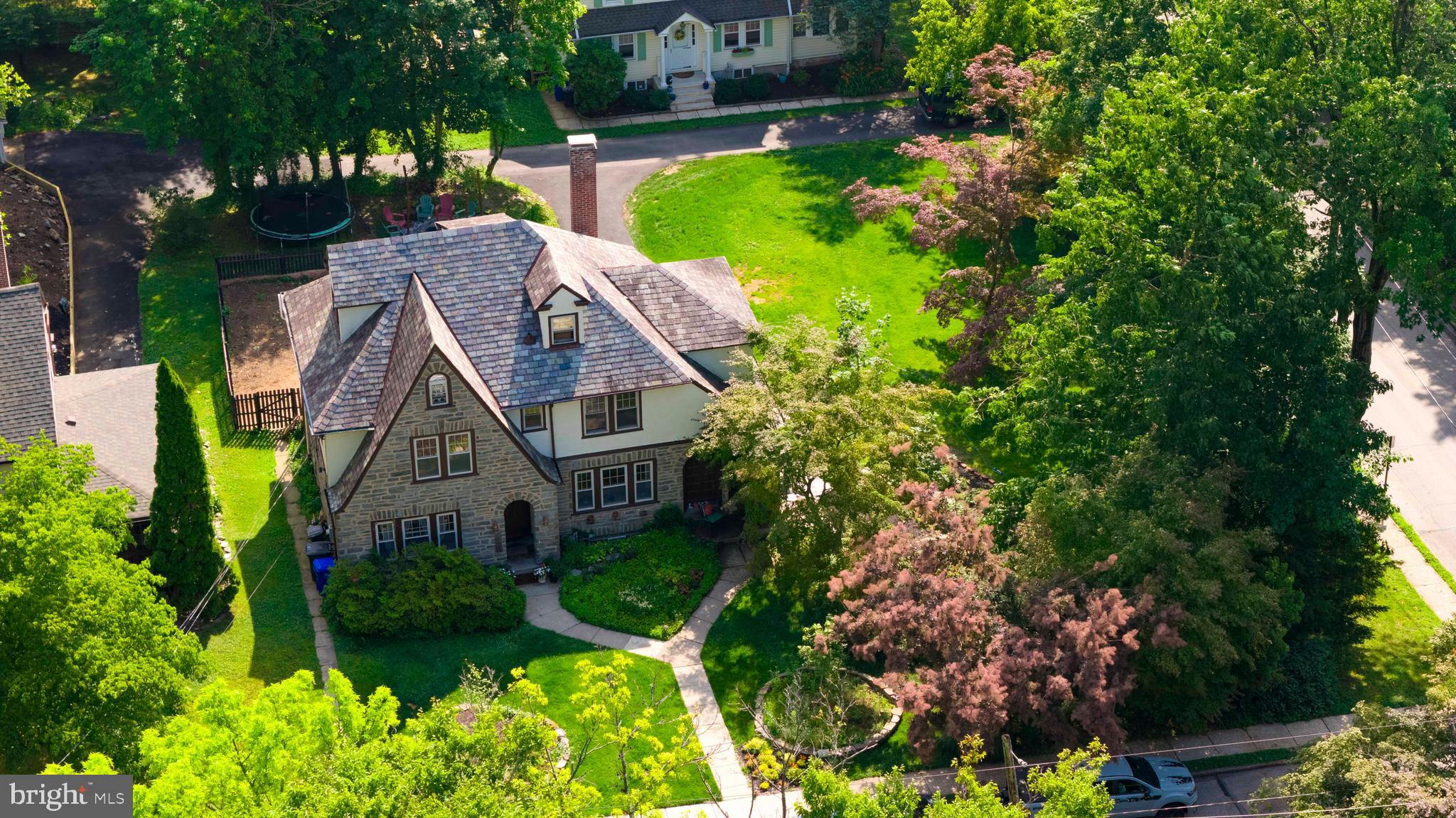 Welcome to 203 Hewett Road, a classic Tudor‑style home set on a large double corner lot with beautifully landscaped gardens in the heart of Wyncote. The property offers timeless character, generous interior space, and a park‑like outdoor setting.

Inviting curb appeal welcomes you inside to a spacious foyer with a central staircase. To the left is the formal dining room connecting to the kitchen, a layout that has served well for everyday meals and holiday gatherings. To the right, a large living room features a wood‑burning fireplace and opens to a screened‑in porch that naturally becomes a favorite spot in warmer months. The porch leads to the deck overlooking the rear yard, creating an easy indoor‑outdoor flow. Beyond the living room, a long bonus room works well as a sunroom, playroom, or studio—space that adapts as life does.

Straight back from the foyer are a half bath and a pantry.

The second floor includes four bedrooms and two full bathrooms, plus an additional room accessed from two of the bedrooms that functions well as a shared study area, nursery, dressing room, or quiet reading space. The third‑floor loft serves comfortably as a fifth bedroom, guest room, office, or private retreat.

The semi‑finished basement includes a separate room suitable for a home gym plus additional hangout space, along with storage, laundry, and walkout access to the rear yard. Outside, the fenced‑in dog run, fire pit area, mature gardens, and open green space offer room for gardening, play, and future enhancements. A newly paved driveway leads to the rear 1‑car garage.

This Wyncote location offers quick access to Route 309, Route 611, and the PA Turnpike, with the Jenkintown–Wyncote Regional Rail Station just minutes away. Parks, restaurants, grocery stores, and everyday conveniences are all nearby.