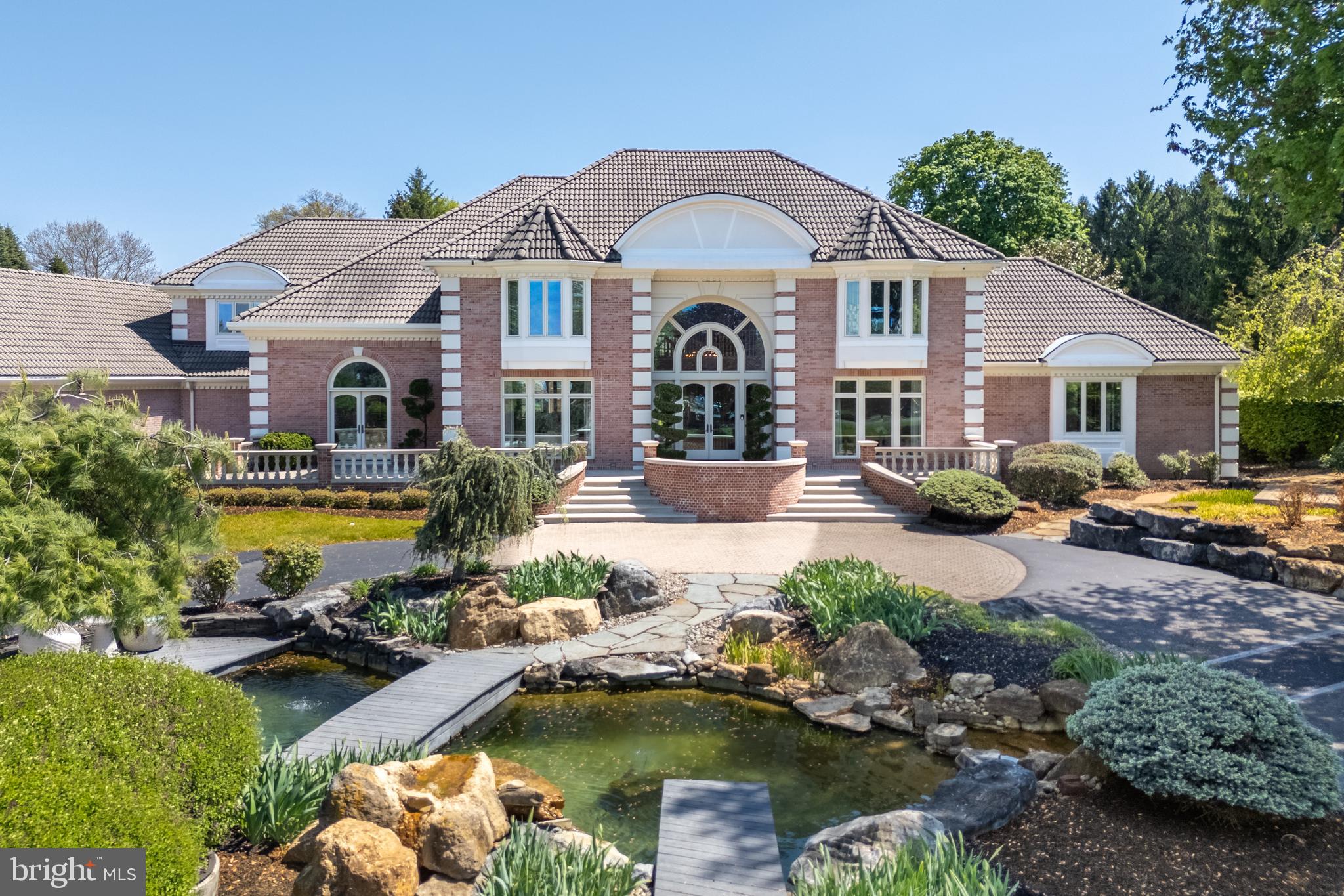 A ONCE-IN-A-LIFETIME ESTATE OFFERING where privacy, refinement, and resort-style living come together in extraordinary fashion. Privately set on 3+ meticulously landscaped acres, this exceptional residence was designed for the most discerning buyer—one who values scale, craftsmanship, wellness, recreation, and a true sense of retreat. Meticulously cared for and maintained, the home makes a striking impression with its double pre-cast concrete balustrade staircase, elegant front approach, and distinctive barrel tile roof. Inside, soaring ceilings, expansive windows, red oak hardwood, Grecian marble tile flooring, custom plaster walls, intricate millwork, and refined architectural details create a home that feels both grand and deeply livable. Designer appointments include Phylrich faucets, Baldwin brass hardware, Hunter Douglas shades, and carefully selected finishes throughout. The floor plan is exceptional, featuring 4 spacious ensuite bedrooms, 5 full baths /1 half bath, a coveted FIRST-FLOOR PRIMARY SUITE, and two private home offices—ideal for today’s luxury lifestyle. The custom chef’s kitchen is beautifully appointed with top-tier appliances, generous workspace, and elegant finishes, offering both performance and style. The walk-out lower level is truly remarkable and expands the home into a complete lifestyle experience. Designed for entertaining, wellness, and relaxation, it features a state-of-the-art gym/fitness room equipped for serious training, a dedicated massage room, a full second kitchen, and expansive recreation and lounge areas that open effortlessly to the outdoor living spaces. Outside, the property becomes a private resort. A stunning salt-water pool with integrated spa, an additional hot tub, two tranquil koi ponds with waterfalls and advanced filtration systems, Mugnaini Italian wood-fired commercial Pizza oven, and a full-sized, Har-tru tennis court create an unmatched setting for VACATION LIVING EVERY DAY. The grounds feel serene, private, and beautifully curated—offering the rare combination of elegance, recreation, and total escape. Ideally located near Northampton Country Club and Moravian Academy, with easy access to Routes 33, 22, and 78, and just minutes to the New Jersey border, this location offers convenience for those traveling throughout the Lehigh Valley, into New Jersey, or toward New York City. This is more than a home—it is a private estate, a wellness retreat, an entertainer’s dream, and a rare opportunity to own one of the area’s most distinctive luxury properties.