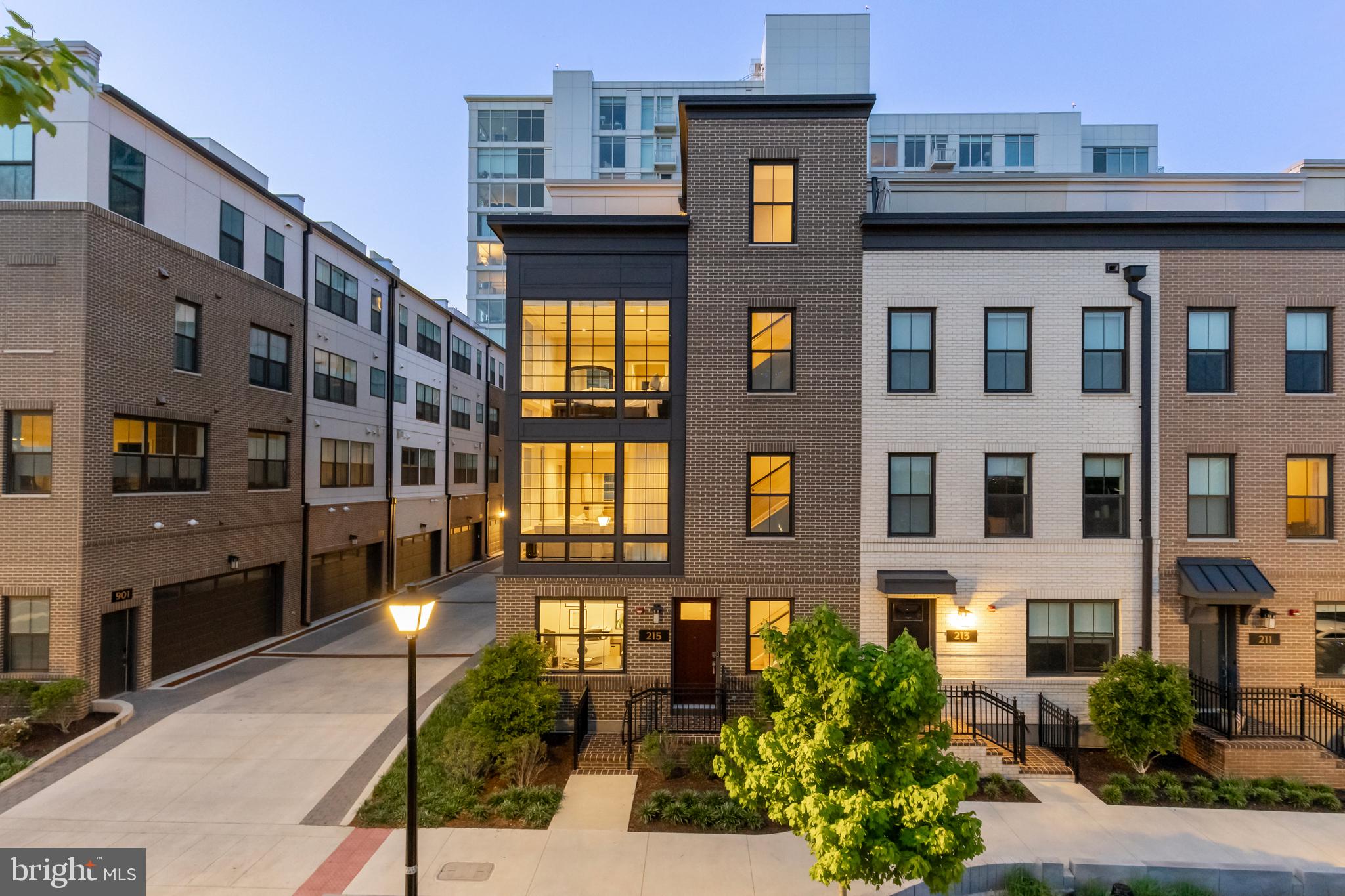Gracing a premium corner lot in Alexandria's sought-after Venue community, 215 Montgomery is a timeless four-level residence just steps from  Potomac River and moments from the  charm of Old Town—The Venue is a masterfully planned enclave of luxury townhomes and condominiums developed by CARR Companies. Positioned on a premium corner lot, 215 Montgomery Street is a stately four-level residence clad in brown brick on all sides, evoking a contemporary reinterpretation of a classic Upper West Side brownstone.

At 24 feet wide and offering 3,344 square feet of elevated living space, the home boasts one of the largest layouts in the community—evoking the sensibility of single-family living within a walkable urban core. A gracious foyer introduces the home, with a private den ideal for welcoming guests, a formal powder room, and access to the extra-wide, attached two-car garage—equipped with EV charging and custom storage solutions.

Ascend via the sweeping staircase or all-level private elevator to the main level, where soaring ceilings and two walls of glass bathe the open-concept floor plan in natural light. Wide-plank oak hardwoods unify the expansive living area, anchored by a striking double-sided fireplace that subtly delineates formal and casual spaces. A second powder room adds additional convenience.

At the heart is a chef’s kitchen designed with clean lines and premium finishes—white shaker cabinetry, a River Rock center island, Calacatta Neve quartz countertops with matching slab backsplash, and a fully integrated Bosch premium appliance suite. A French door wine cooler adds a refined touch.

The upper-level primary suite is a true sanctuary, spanning half the floor and featuring dual custom walk-in closets and a dedicated dressing area. The lavish bath showcases a double River Rock vanity, Bianca Carrara matte flooring, a large glass-enclosed shower, and a separate water closet. Past the side-by-side laundry closet, a secondary bedroom enjoys its own ensuite bath with chic tiling and a walk-in glass shower.
The top level offers a third bedroom with ensuite bath, a cozy loft lounge, and access to the home’s pièce de résistance—a private rooftop terrace with a custom kitchen and  panoramic views of the Potomac and the National Harbor, MD skyline.

Smart home features abound, including Ubiquiti Networking and Savant Home Automation, Ring security, Sonos in-ceiling audio, Lutron motorized window treatments, Ecobee smart thermostats, Samsung, Sony and LG wall-mounted TV's, and Kohler electronic bidets throughout.

Set moments from the Mount Vernon Trail, MetroStage, and Old Town’s beloved shops and eateries, 215 Montgomery Street presents an unrepeatable opportunity to enjoy an innovative, luxurious urban lifestyle in the heart of Alexandria.