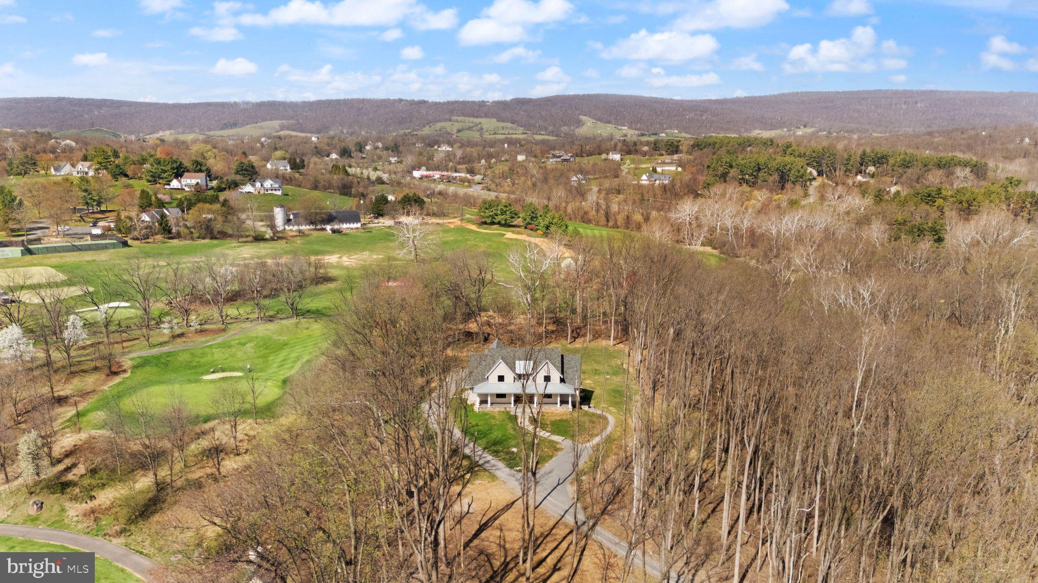 Modern Farmhouse Property in Beautiful Western Loudoun County

 MAJOR PRICE REDUCTION! NOW OFFERED AT $1,899,000

OVER $200K OF UPGRADES SINCE ORIGINAL PURCHASE!

This exceptional Nearly New Custom Home offers refined luxury and privacy on an elevated 5.2-acre wooded homesite bordered by protected Open Space and Stoneleigh Golf & Country Club. The setting is peaceful and scenic, with seasonal mountain views, mature trees, and a tranquil creek. NEW LANDSCAPING JUST INSTALLED.  Located just 1/2 mile from Round Hill and minutes to Route 7, the property provides both seclusion and convenience, along with no HOA, underground utilities, and high-speed Verizon Fios.
A private quarter-mile driveway leads to the stone and Hardi-Plank exterior, where the wraparound porch and curated hardscaping create a striking arrival. Inside, the home features 10-ft ceilings on the main floor and 9-ft ceilings on the upper level and basement, along with White Oak wide-plank wood floors, soaring beamed accents, a dramatic floor-to-ceiling stone gas fireplace, and a formal library with French doors. Large windows and an open layout highlight the natural surroundings and create a warm, elevated atmosphere and lovely views from every room.
The main-level Owner's suite offers a luxurious retreat with a custom closet including an island and window seat, a spa bath with heated floors, oversized walk-in shower, soaking tub, and toilet closet. Direct access to a covered porch with a gas fireplace extends the suite into a year-round outdoor living space.
The chef's kitchen is equipped with a Wolf range, Subzero refrigerator, Bosch dishwashers, Designer Level 5 Granite island, ceiling-height cabinetry with lighted glass uppers, walk-in pantry, and Butler's pantry. The main level also includes an open elegant dining area, a corner pocket office, the Great Room with Stone Gas Fireplace that leads to the rear covered porch, a full tiled bath and walk-in shower, and a mudroom/laundry with built-ins and access to the 3-car garage.
Upstairs offers a loft and media area with a wet bar and beverage fridge, plus three bedrooms-one ensuite and an additional full hall bath, which can be shared by loft area visitors and the two extra bedrooms.
The fully finished basement features high ceilings and includes a fifth ensuite bedroom, a hobby room with workbench, a large family room with an entertainment bar and full-size refrigerator, and a walkout to the custom patio and hardscape path to guest parking.
Premium upgrades include custom built-ins, designer window shades, High-End Systems, deluxe appliance and paint packages, upgraded blown-in insulation, 8 Ceiling Fans, a 500 GAL buried propane tank, and a whole-house generator. Close to Purcellville, Leesburg, wineries, breweries, parks, pools, and shopping, with Dulles Airport approximately 35 minutes away.

Current school district includes Woodgrove High School, Harmony Middle School, Mountain View Elementary. Check for updates, as districts change occasionally.