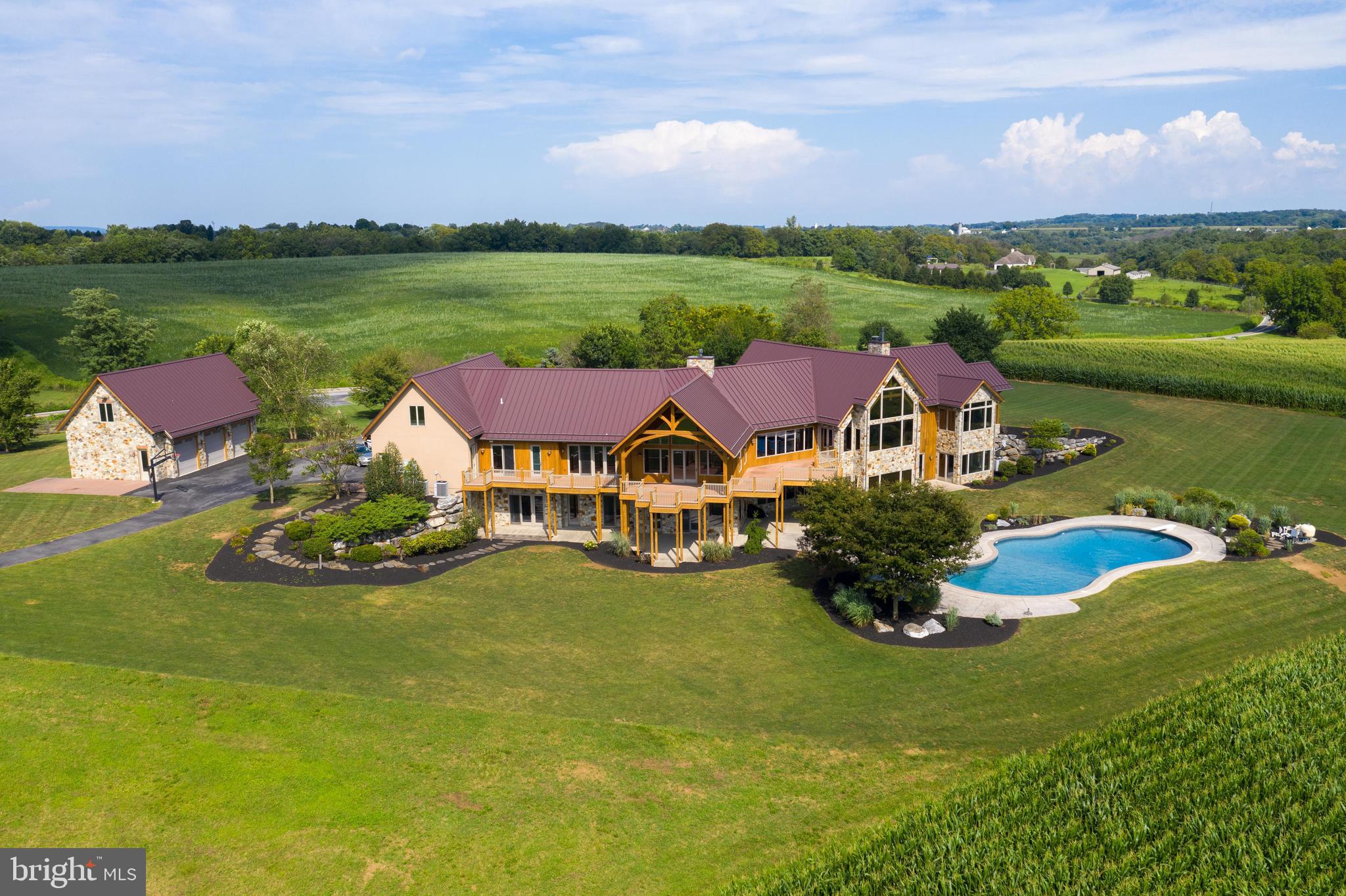 CLICK THE VIDEO ICON TO TOUR THIS HOME.  This magnificent home with nearly 11,000 square feet of living space is situated perfectly on a private 87 acre lot that includes 4 separate pastures.  This one-of-a-kind home with 6 bedrooms and 5.5 bathrooms features 4 stone fireplaces, stunning beech wood flooring, and beautiful exposed beams and soaring ceilings throughout. Open concept floor plan flows effortlessly between great room, dining space, and a gourmet chef's eat-in kitchen which features granite countertops, double oven, and new cooktop.  Spacious master suite with vaulted beam ceiling, sitting area, large walk-in closet, and walk-out patio features a beautiful master bath with soaking tub, tile shower, and dual vanities with recessed lighting.  Additionally the home includes family room with wet bar, library with custom built-in shelving, and mud room.  Finished lower level has a summer kitchen and theater room with tiered seating that includes equipment. Enjoy breathtaking views of the sprawling land from the large rear deck, patio, and heated in-ground pool, which provide a picturesque setting for entertaining.  The professionally landscaped lawn enhances the natural beauty of the lot, and creates lots of shade from the mature trees.  There is ample parking between the attached 3-car garage, and additional detached 3-car garage.