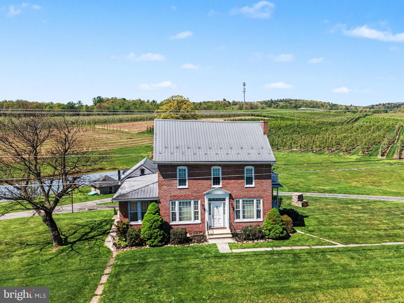 What a beautiful place to call home! This timeless 3-bedroom brick farmhouse sits on a picturesque 2.6 acre lot in the heart of Apple Country, complete with a large private pond and panoramic orchard views. This spacious home features a warm and inviting floor plan, a large eat-in kitchen with floor to ceiling oak cabinetry, a spacious living room perfect for entertaining family and friends, a separate dining room, a bright sunroom, a half bathroom, and a versatile main-floor bonus room ideal for an in-home office, playroom, or gym. Upstairs you'll find three bedrooms with beautifully refinished hardwood floors, a main bathroom, and a bonus room with a charming balcony. The home features a walk-up attic perfect for storage. Numerous major updates have been completed since 2018, including a new metal roof, new windows, a new furnace, a new hot water heater, a well pump, and a new 200-amp electrical panel, all offering peace of mind for years to come. Enjoy fishing in your own pond, relaxing and taking in the views of nature year-round, and plenty of space for hobbies and storage with a detached garage and multiple outbuildings. Upper Adams Schools, and conveniently located just minutes from town and a short drive to Carlisle and historic Gettysburg. This one won't last long! Schedule your private tour today!
