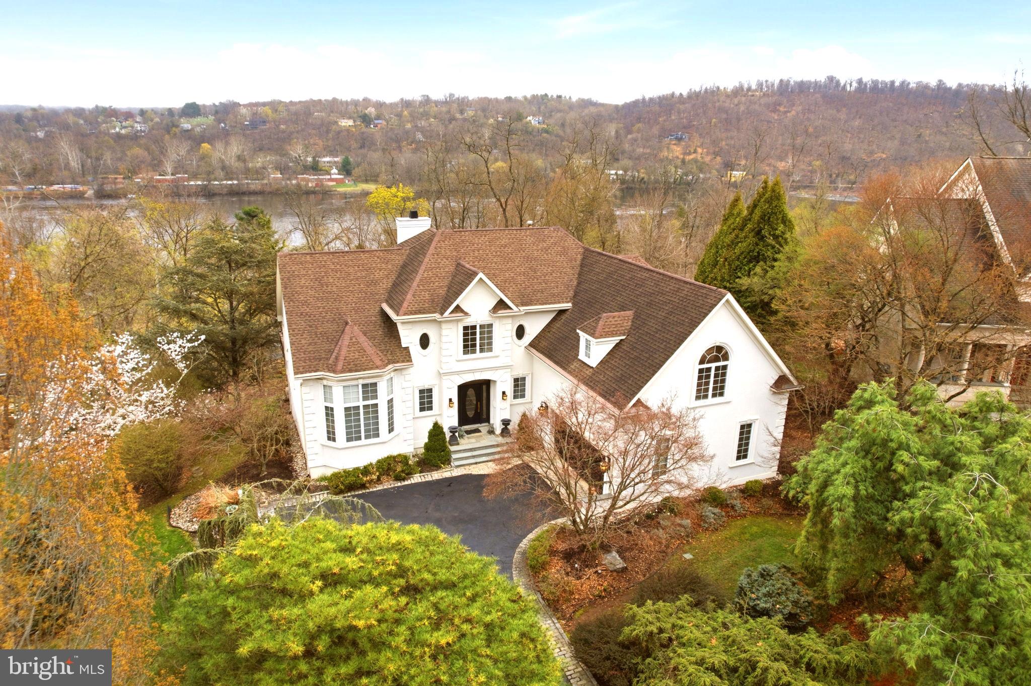 Known as “The Belgravia of New Hope,” this refined residence is located above New Hope Boro, offering convenient access and walkability to the vibrant downtown area. The property presents an ideal combination of space, comfort, contemporary design, and appealing aesthetics. Seasonal river views enhance the setting, whether enjoyed from the expansive deck, paver patio, or through numerous Andersen windows. The home features three levels with abundant natural light, high ceilings, and thoughtful amenities throughout. The gourmet kitchen is equipped with a commercial-size Electrolux refrigerator, warming drawer, beverage refrigerator, and a large center island with extensive preparation space. The first-floor primary suite includes generous storage options with three spacious walk-in closets, one of which provides seasonal river views and direct access to the deck. The mezzanine level offers three additional bedrooms, a full bath, a living area, and a dedicated workspace. A finished walkout lower level provides versatility for independent guest accommodations or other personalized uses. Additional highlights include a whole-house generator, newer HVAC system, newer water heater, and over $300,000 in improvements. The home is set on a private, scenic lot and features a clean, neutral palette and timeless design.
