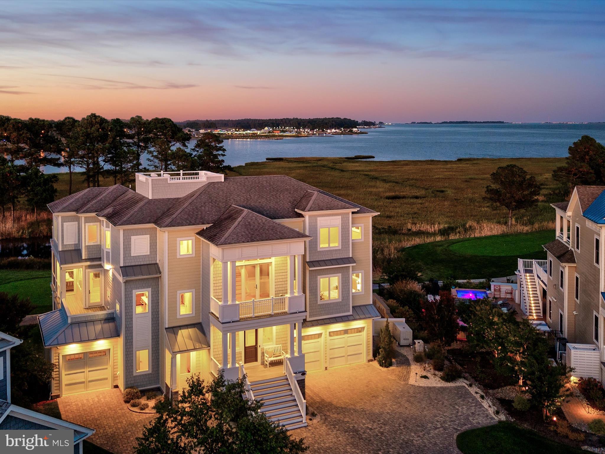 A Sanctuary of Coastal Elegance with Endless Views
A one-of-a-kind masterpiece by Echelon Homes, this custom-designed residence marries contemporary coastal style with subtle industrial cues, delivering awe-inspiring luxury at every turn. Nestled within the prestigious Jack Nicklaus Signature Golf Course community of The Peninsula, this extraordinary home rises in the exclusive Sanctuary enclave, perched on the pinnacle of Sand Dollar Drive. Designed to maximize its spectacular position, the residence offers three levels of living with sweeping 360-degree views of the Indian River Bay, Lingo Creek, and the 8th Tee.
From the moment you arrive, casual elegance blends seamlessly with quality craftsmanship and coastal sensibility. Wide-plank hardwood floors, shiplap, judges paneling, beamed ceilings, and custom built-ins unify the interiors, while designer lighting adds glimmering sophistication. The main level foyer opens to the great room, where floor-to-ceiling atrium sliders flood the space with natural light, showcase breathtaking views, and extend effortlessly to an expansive balcony deck. The living room is anchored by a soaring quartz-clad fireplace, accented with black steel and flanked by elegant glass-and-wood display cabinets. An open-beamed ceiling heightens the drama, creating a stunning focal point. This central gathering space flows into the gourmet kitchen and dining area, a showcase for both entertaining and daily life. Quartz surfaces span generous work areas and the oversized center island, complete with abundant storage, beverage and wine refrigerators, deep undermount sink, and built-in oven. A striking glass tile backsplash highlights the GE Monogram six-burner range with custom vent hood, while a suite of professional-grade stainless appliances completes the space. A walk-in pantry with custom floor-to-ceiling storage ensures both beauty and function. Dine casually at the breakfast bar, host formal meals in the adjacent dining room, or step through sliders to the screened porch, where dazzling sunsets over the bay make every evening extraordinary. This level also offers a refined home office with balcony access, a stylish hall bath, and the first of five bedrooms, complete with ensuite. Ride the elevator to the primary suite retreat, where panoramic views greet you from bed beneath a soaring cathedral ceiling of shiplap and beams. The spa-inspired ensuite rivals a five-star resort, with two vanities, soaking tub, walk-in shower, private water closet, and dual walk-in closets with abundant storage. Two additional guest suites, each uniquely styled with private ensuites, one with balcony access, ensure comfort for family and friends. A second-floor laundry adds convenience, while a welcoming family room with balcony access serves as the perfect gathering spot. From here, a staircase leads to a bonus loft and the crowning jewel of the home: a rooftop terrace offering unrivaled 360-degree views. The lower level, filled with natural light, high ceilings, and precise millwork, is designed for entertaining. A game and lounge room, sizable guest bedroom, hall bath, second laundry, and mudroom entry complement the oversized two-car garage and additional third garage. Beyond the garages, a pool bath leads to the outdoor oasis. Here, a hardscaped paradise awaits: heated pool, spa, firepit, lounging areas, covered bar patio, and a screened pavilion, all perfectly positioned to embrace the home’s remarkable setting.
As a resident of The Peninsula, you’ll enjoy world-class amenities, including gated security, a stunning clubhouse, the Jack Nicklaus golf course and driving range, a state-of-the-art fitness center with indoor, outdoor, and wave pools, hot tubs, saunas, spa rooms, tennis and pickleball courts, dog park, community garden, nature center, bay beach, fishing pier, and miles of walking trails.
Come home to comfort, luxury, and resort living at its finest.