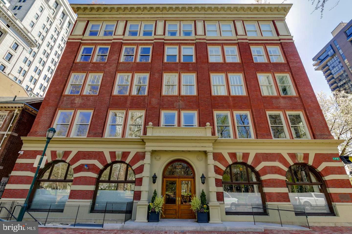 Before we entice you with the wonders of this beautiful residence, it’s important to note that the Lippincott is one of the few original buildings of distinction that line Washington Square. At one point in time, it was the largest publishing house in the world. And Washington Square has been, & still is, one of the most coveted locations in Philadelphia. Now for your tour:  Enter the  Residences  of the Lippincott through a tasteful newly upgraded lobby, hosted by a 24-hour concierge/door person(s).  Take the private elevator & arrive directly into the foyer of your home.  As you enter the residence, there are a few things you will immediately take note of, they include: the gorgeous wood flooring that runs throughout, the neutral & soothing paint tones & the glorious, bright, open & airy floor plan. If you enjoy natural sunlight, you will love this property! Stroll to your right down a short hallway which opens-up to a kitchen, dining room & living room combination. The kitchen boasts endless quartz countertop space, including a large eat-on section with barstool seating. There are stainless steel appliances including a commercial grade Wolf oven & a Subzero refrigerator, & a tasteful tile backsplash. This kitchen is designed for the most discerning of chefs! The dining room is large & can accommodate multiple guests at your holiday get togethers. The living room is nothing less than magnificent, in part because its original exposed brick walls give it charm and character. It is also home to your gas fireplace which sets the stage for both entertaining and relaxation.  From the living room there’s a door that leads you to your full-length back porch with wonderful Eastern views including treetops & your morning sunrises. This is the perfect place to sip your morning coffee & enjoy your evening glass of wine. Just off the living room there is a bonus room which can be used as a library, billiard room, or an expansive office. Until recently it was used as a music room and was home to a grand piano. Like the living room, it also boasts the charm of floor to ceiling brick walls & has a separate door leading out to the porch.  As you may have noticed as you walked through all the aforementioned rooms & as you continue on with your tour, every room in the house has high and tray ceilings  with tasteful definitions. This home provides you with three bedrooms and three full bathrooms. One of the bedrooms has an en-suite. The master bedroom is nothing less than grand. It has two walk-in closets (plus a wall of additional closet space) & a gorgeous master bathroom with two vanities separated by a large jetted soaking tub & a wonderfully tiled private shower. This property continues on to a wide spiral staircase that takes you up to a foyer with multiple skylights & two sets of sliders to your expansive rooftop deck. Here you will find a degree of privacy and the perfect place to either entertain or unwind. There are many honorable mentions to this property that will be experienced when you take your tour. The residences at the Lippincott just completed a full interior upgrade of the main lobby, floors & hallways & our unit unit has a New HVAC System that will be installed before you move in! There a comfortable & well-equipped gym & this unit comes with two ample-sized indoor parking spaces & an expansive storage room. The garage also boasts EV Charging Stations for both of your parking spaces. Lastly, this property’s location provides you w/unlimited inner-city conveniences. Walk out the front doors of the lobby & directly into one of the most gracious city parks in Philadelphia. Just a stroll in any direction will lead you to shopping venues, fantastic eateries, jogging & biking trails, dog parks, theaters, the arts, historic sites galore, area hospitals & immediate access to unlimited public transportation venues. Everything is literally at your fingertips! Do not hesitate. Schedule the personally guided tour today!