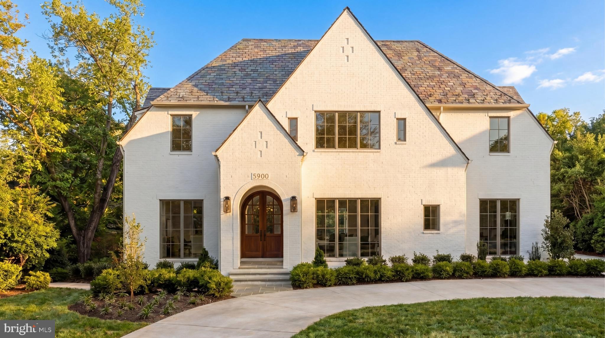 Prominently sited on a prestigious corner lot in the heart of coveted Kenwood, 5900 Kennedy Drive stands as the newest architectural triumph by Terra Innovations, created in collaboration with the acclaimed GTM Architects and the master craftsmen at Castlewood Builders. Conceived as a transitional Tudor, the residence is clad in crisp white brick, an enduring design that merges time-honored English traditions with a contemporary sophistication perfectly suited for modern living.

The home has been deliberately oriented to capture southern exposure, allowing natural light to flood the principal rooms. A unique detached one-car garage complements the concealed two-car side-load garage, maximizing lot usability while preserving green space. A sweeping driveway introduces the stately façade, defined by steeply pitched gables, a slate-style roof, and an arched mahogany-and-glass entry door. Inside, a subtly vaulted foyer sets the stage for 8,808 finished square feet across four thoughtfully designed levels.

A classic center-hall plan anchors the main floor. To one side lies the formal living room, light-filled and inviting. To the other, the dining room is distinguished by a tray ceiling with cove lighting, setting a refined tone for entertaining. A private study with custom built-ins offers a serene retreat and, with access to a full bath, doubles as a main-level bedroom—an ideal option for multigenerational needs.

The open-concept family room forms the heart of the residence, crowned by dramatic ceiling beams and a gas fireplace framed by built-ins. Expansive glass doors open to the covered porch with its own fireplace, pre-wired for screens, heaters, and media, blurring the line between indoor and outdoor living.

At the center of the home is the chef’s kitchen, anchored by a 9-foot artisan island and outfitted with bespoke cabinetry, stone finishes, and top-tier hardware. The 55” Lacanche Classique range serves as both a culinary tool and centerpiece, complemented by GE Monogram appliances. A concealed coffee bar, butler’s pantry, and sunlit breakfast area complete the space. Everyday functionality is enhanced by a mudroom wing with powder room, pantry, laundry hookup, and garage access.

Upstairs, the primary suite offers a sitting area, private terrace, and dual walk-in closets with custom built-ins. The spa-inspired bath features heated floors, a freestanding soaking tub, dual vanities, and a Kohler digital shower. Four additional en-suite bedrooms and a laundry room complete this floor. The top level adds another bedroom, full bath, and family room, all accessible by the home’s four-level elevator.

The lower level is indulgent yet functional. A 32-foot recreation room with wet bar and glass-enclosed wine display serves as its centerpiece. Wellness amenities include a fitness studio, steam shower, and sauna, while a pre-wired golf simulator bay with raised ceilings offers versatility as a recreation or media room. A private au pair suite with exterior access provides independence and flexibility.

Outdoors, the level rear lawn is private and pool-ready, with infrastructure already in place. The home’s location is unmatched, set among Kenwood’s famed cherry blossoms, across from the revitalized Westbard Square, minutes to Downtown Bethesda, and near top-rated schools and commuter routes.

A singular achievement in design, craftsmanship, and livability, 5900 Kennedy Drive establishes a new pinnacle of luxury in one of the Capital Region’s most distinguished neighborhoods.