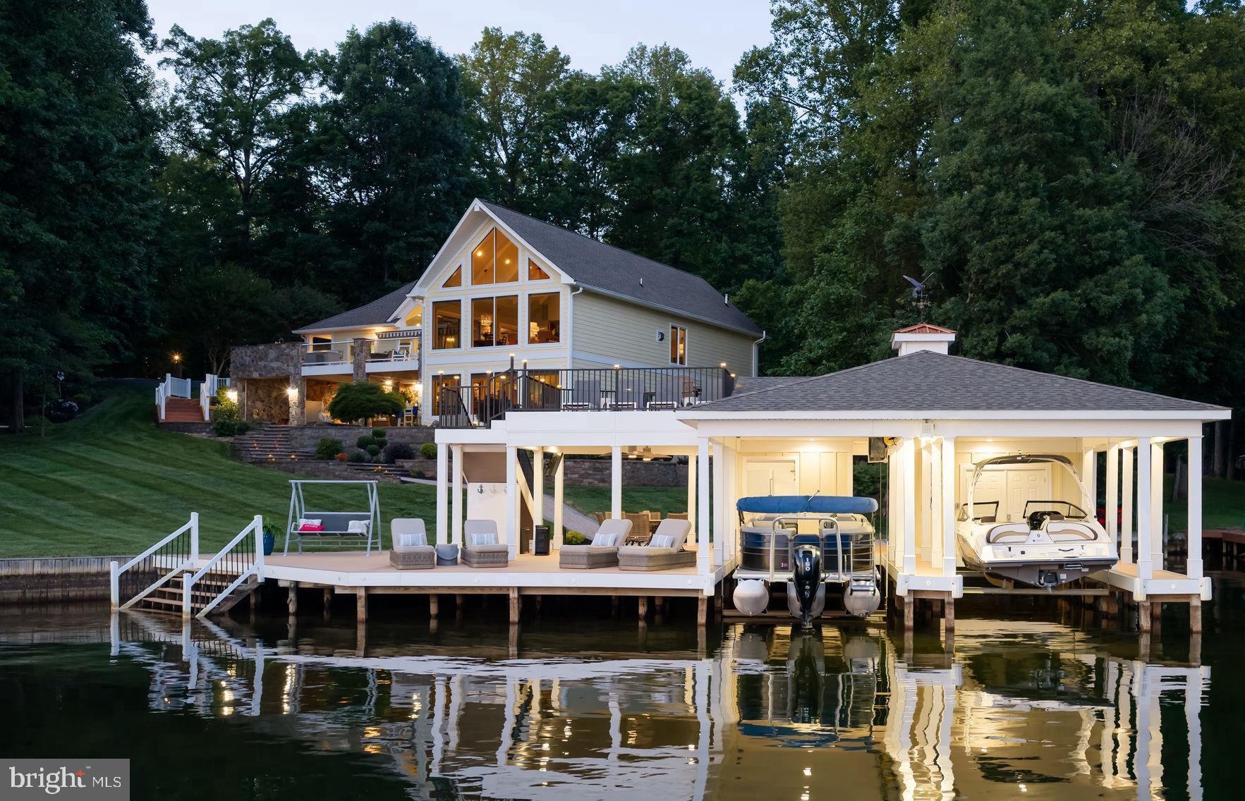 Luxury lake living reaches a whole new level at this extraordinary waterfront estate on the private side of Lake Anna. Offered fully furnished and completely renovated from top to bottom in 2022, this custom home is perfectly positioned in the highly sought-after Both Waters Estates community and offers nearly 6,000 square feet of meticulously crafted living space, breathtaking wide-water views, and an unmatched collection of upgrades inside and out. Set on 1.05 acres with approximately 240 feet of pristine bulkheaded shoreline, deep water, and some of the most spectacular views on Lake Anna, this is a rare opportunity to own a true lakefront masterpiece. Designed to maximize the incredible waterfront setting, the home features 5 bedrooms, 4 full baths, 2 half baths, and multiple indoor and outdoor living spaces perfect for entertaining and relaxing. Vaulted wood ceilings, custom built-ins, Amish-crafted cabinetry throughout, designer finishes, and stunning lake views create an unforgettable first impression. The spacious living room showcases a shiplap-accented fireplace, while the large family room is anchored by a dramatic double-sided stone fireplace and framed by unobstructed water views that seem to stretch for miles. The gourmet kitchen was designed for both everyday living and entertaining, featuring custom Amish cabinetry, quartz countertops, a large center island, high-end Thermador appliances, a Miele dishwasher, a 6-burner gas cooktop, wall oven, and a separate wet bar complete with Silestone countertops, ice maker, and beverage cooler. The spacious main-level primary suite features vaulted ceilings, a double-sided stone gas fireplace, electric blackout shades and a custom walk-in closet with built-ins. Radiant heated flooring, a double vanity, barn door accents, and a luxurious tile walk-in shower. The walkout lower level offers a second primary suite with its own private bath, additional guest bedrooms, and plenty of room for family and friends to spread out and enjoy lake life. Step outside and you'll quickly understand what makes this property truly special. Extensive hardscaping, stone columns at the entrance, a paved driveway, professional landscaping, exterior lighting, lake-fed irrigation, and multiple outdoor gathering spaces create a resort-like atmosphere. The upper deck features stamped concrete flooring and glass-panel railings that allow the lake views to take center stage. The covered lower patio is waterproof and equipped with built-in electric screens, creating the perfect outdoor living space year-round. A built-in outdoor kitchen with grill and ceramic-style smoker, fire pit area, and oversized entertaining spaces make hosting effortless. The showpiece of the property is the incredible custom boathouse completed in 2024. Designed for serious lake enthusiasts, it features two covered slips with electric lifts, composite decking, upper and lower sun decks, a tiki bar with serving window, storage room, double jet ski pad, tankless water heater, and an outdoor shower. Spend your days boating, swimming, and entertaining, then go out & anchor your boat for the spectacular Fourth of July fireworks over Dike 2. Additional features include Firefly Fiber internet, an oversized attached two-car garage, a 24x24 workshop with electric and window unit, an additional storage shed, three Trane HVAC systems with filtration systems, and three Rinnai tankless water heaters. Both Waters Estates offers something no other Lake Anna community can match; exclusive access to both the private and public sides of the lake. As an added bonus, this property includes its own assigned boat slip on the public side in the community common area, giving you unrestricted enjoyment of everything Lake Anna has to offer. Luxury, craftsmanship, location, and unforgettable views come together in this timeless waterfront estate. An exceptional property that truly represents the very best of Lake Anna living.