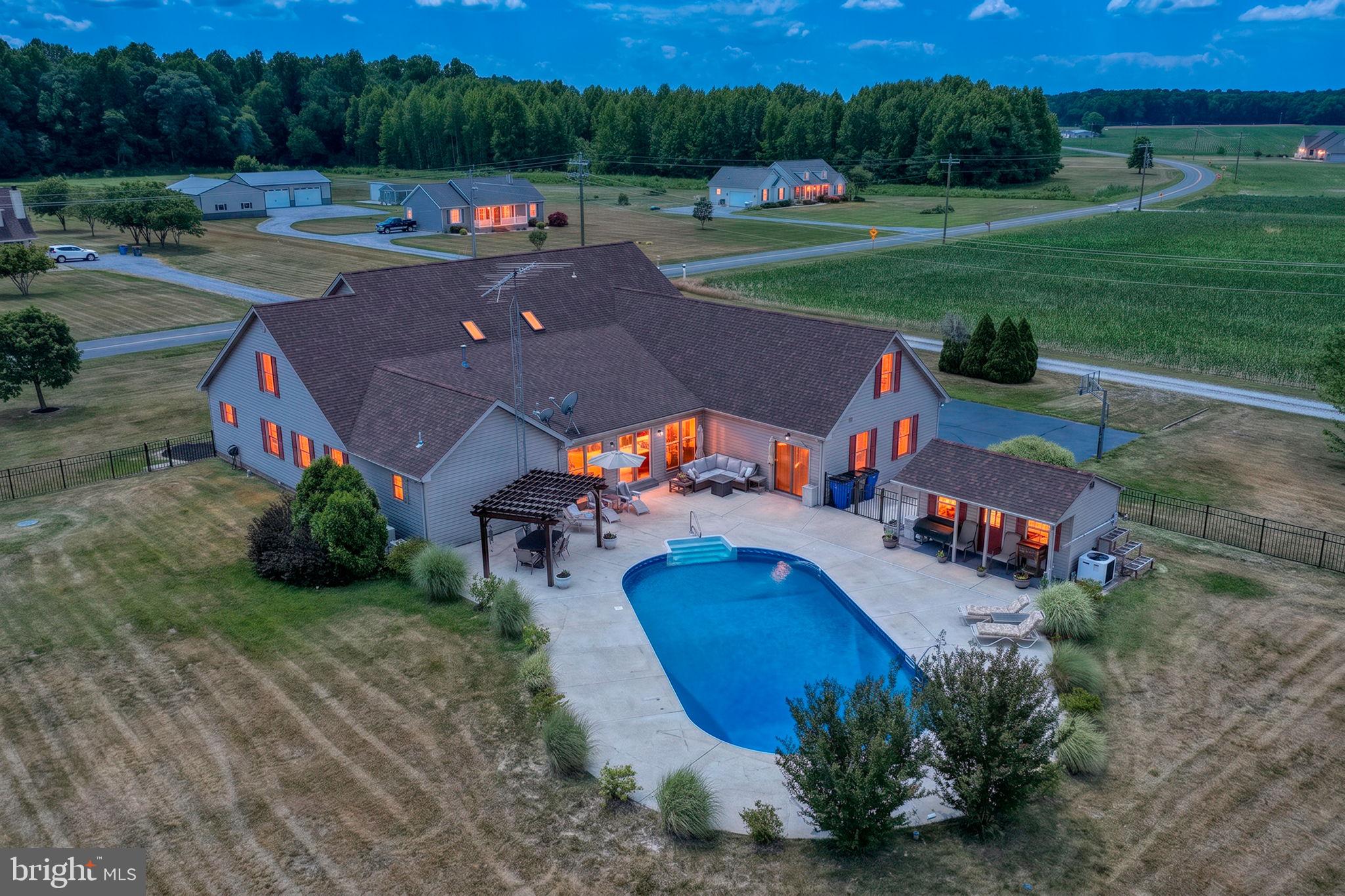 Welcome to your own private retreat on 2 beautifully landscaped acres surrounded by peaceful farmland views. This impressive 5-bedroom, 3-bath home offers over 4,100 square feet of living space designed for both everyday comfort and entertaining. A charming wraparound porch welcomes you home and provides the perfect place to relax and take in the peaceful country setting. The heart of the home is the expansive eat-in kitchen, featuring abundant cabinetry, generous prep space, and plenty of room for gathering with family and friends. Multiple living areas include a dedicated office, an oversized sunroom filled with natural light, a spacious living room, and an upper-level loft, providing flexibility for every lifestyle. The first-floor primary suite offers two spacious closets and a custom ensuite bathroom. Two additional first-floor bedrooms are connected by a Jack-and-Jill bathroom, creating a functional layout for family or guests. Upstairs, you'll find two generously sized bedrooms, a full bath, and a large sitting area perfect for a second living space, game room, or guest retreat. Practical features abound, including a dedicated laundry room with built-in cabinetry and a three-car garage complete with storage and workshop space. Step outside to experience your own backyard oasis. The expansive patio surrounds a sparkling in-ground pool and pool house, creating the perfect setting for summer gatherings and outdoor entertaining. A black iron fence adds both beauty and security, while the surrounding farmland provides exceptional privacy and picturesque views in every direction. Combining space, functionality, and resort-style outdoor living, this one-of-a-kind property offers the rare opportunity to enjoy country serenity without sacrificing modern conveniences.