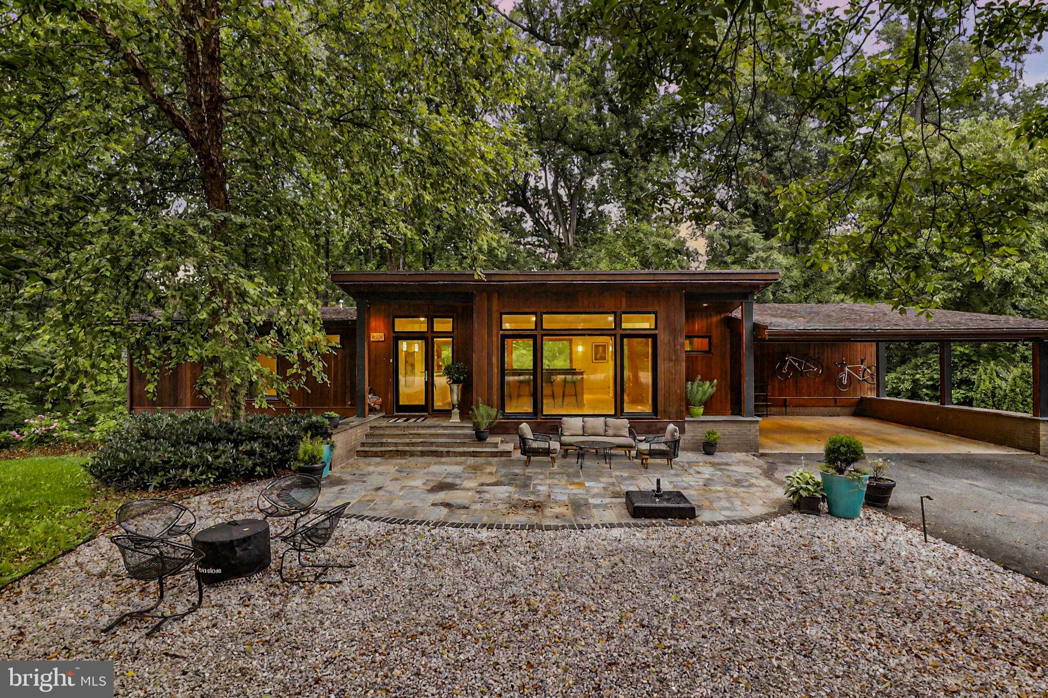 Welcome to 6921 Ayr Ln, a hidden gem tucked away at the top of a peaceful cul-de-sac in the heart of Bannockburn. This exclusive enclave of just 10 homes offers unmatched privacy and tranquility. Nestled beside a wooded lot, the property enjoys a lush, green backdrop—your own private sanctuary in an exceptional natural setting.

This contemporary retreat is a seamless blend of timeless design and modern luxury. With three spacious bedrooms, two and a half beautifully appointed bathrooms, and set on 0.42 acres, the home delivers effortless comfort and sophisticated style. Clean architectural lines, open-concept living spaces, and walls of glass flood the interior with natural light, creating a strong indoor-outdoor connection.

From the street, the home maintains a quiet, refined presence—defined by original wood siding, crisp geometry, and a canopy of mature trees that echo its Mid-Century Modern roots. Step inside, and the atmosphere transforms. Sunlight pours through expansive windows, and the interior opens into a bright, serene escape that invites relaxation and inspires connection.

Whether you’re enjoying peaceful solitude or entertaining with ease, 6921 Ayr Ln is a rare opportunity for modern living in an unparalleled setting.

The main entry level opens into a welcoming flex space directly off the carport. At the center of the home is the open-concept kitchen—featuring custom cabinetry and premium Wolf and Sub-Zero appliances—that flows seamlessly into the adjacent dining and living areas. Laundry and pantry areas are located directly behind the kitchen, making them both convenient and user-friendly. The sun-drenched living room—with its gas fireplace and built-in bookshelves—adds warmth and personality. Designed for everyday living and casual gatherings alike, this space brings people together with ease and comfort.

Two generously sized bedrooms, a stylish powder room, and a full bathroom with dual vanity complete this level—perfect for guests, family, or flexible use.

The garden level, bathed in natural light and with direct access to the backyard, expands the home’s livable space in a thoughtful, functional way. At its heart is a spacious family room with oversized picture windows and a wood-burning fireplace with gas hookup—perfect for cozy evenings, lazy weekend mornings, or casual entertaining. This level also features a private en suite bedroom, complete with wood-paneled ceilings, a built-in desk, a dressing nook, and a sleek bath with an oversized walk-in shower. A wet bar, custom built-ins, and two large storage rooms round out this versatile floor.

Outside, the magic continues. Step into a vibrant community with two neighborhood pool clubs, one just minutes away via a charming wooded path at the end of the cul-de-sac. Located in the highly sought-after Walt Whitman school district and close to walking and hiking trails, this home is just a short drive to Downtown Bethesda, Potomac Village, Whole Foods, and Washington, D.C.

With beloved neighborhood traditions like Food Truck Fridays and an annual talent show, Bannockburn is more than a location—it’s a true community. And 6921 Ayr Ln is your chance to be part of it.