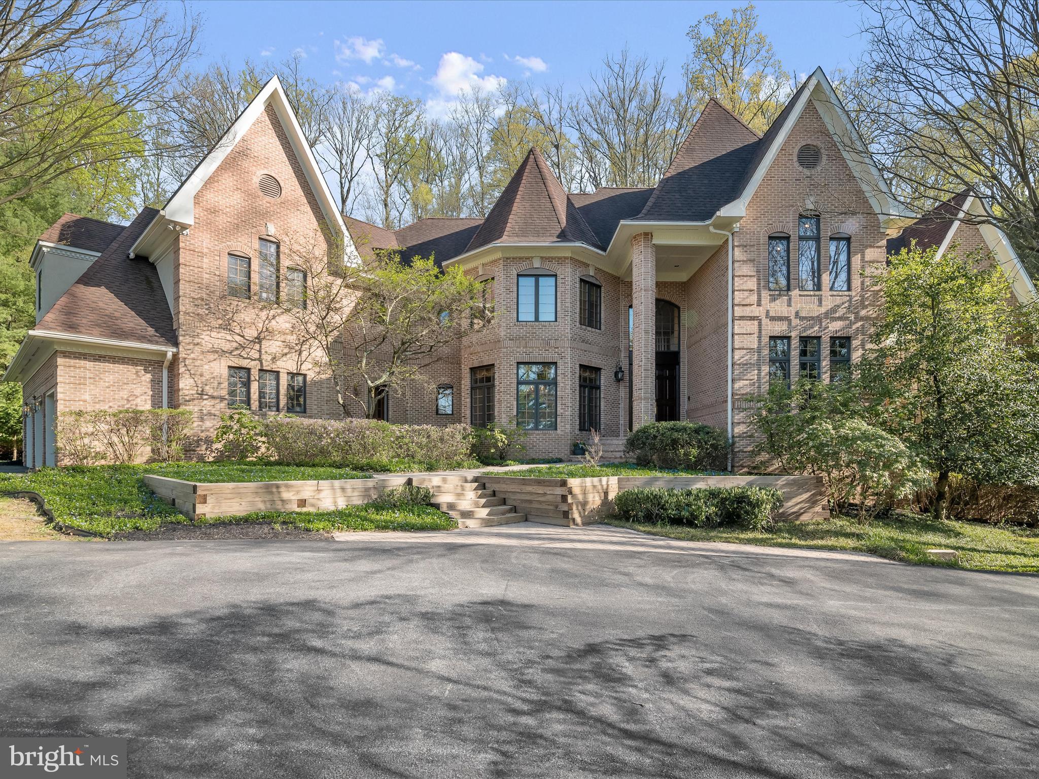 Perfectly situated on a premier lot overlooking Greenspring Valley, this quintessential French Manor home is encircled by seasonal blooms, expert landscaping, hardscaping, and outdoor living that, together, take full advantage of the majestic setting over which it presides. Inside, the architectural details include neutral interiors, immaculately maintained hardwood floors, arched headers, French window transoms, and spaces designed with the symmetry of French turrets. Cascading garden beds and a stately front elevation draw you into a covered brick porch, while a pair of solid wood entry doors welcome you inside.
A two-story foyer unfolds into a dramatic open plan and octagonal dining room with built-in buffet cabinetry. An extended central foyer is adjacent to the formal living room defined by a soaring two-story ceiling, a wall of stacked windows, atrium French doors to the outdoor patio, and a wood-burning fireplace sided by finely finished built-ins.
Exquisite French Manor Home with Premier Lot Overlooking Greenspring Valley
Perfect for main level living, a primary bedroom suite with sitting room, French doors to brick patio, an upgraded luxury bath with designer finishes, boasts an oversized walk-in shower, soaking tub, two vanities, and three walk-in closets. Adjacent to the primary suite wing is a formal study outfitted with richly finished library shelving, and a formal powder bath.
Idyllic indoor and outdoor entertainment is enhanced by the serene setting and plantings outside and is supported inside by the open floor plan and circular traffic flow that continues into the family room and kitchen. Indoor entertainment in the family room offers a convenient wet bar and a commanding stone fireplace. French atrium doors in both the family room and in the adjoining breakfast room will invite friends and family to meander outside and take in the beauty of outdoor venues accessing the brick patio and the low maintenance dining deck seamlessly.
The adjacent upgraded kitchen offers a spacious walk-in pantry, up-to-the-minute 12 x 24 designer floor tile, a center island, cook station, and breakfast bar wrapped in fresh white European cabinetry accented with feature designer hardware. The kitchen is purposefully designed as the heart of the home and is conveniently encircled by several important access points. In addition to the formal dining room and exterior dining deck, the kitchen offers access to the laundry room, mudroom, secondary covered entry, secondary powder bath, garage, and secondary back stair.  At the top of the stairs, four additional en-suite bedrooms and a walk-in cedar closet encircle a spacious game room with two generous built-ins. 
Living spaces and amenities abound on all levels, including the lower level that is ready to finish. Generously sized, light-filled spaces, walk-out doors to a rear patio, daylight windows, a two-sided brick fireplace, a bath plumbed for steam shower, and an excellent waterproofing system are already in place and waiting to be finished according to your specifications. Come home to meticulously maintained luxury, a beautiful setting with serene outdoor spaces, and a very special lifestyle inside with main level living flexibility and room to grow! 5 minutes to I-695 , less than 10 min. to shopping center , Trader Joes & more. Convenient to all amenities.