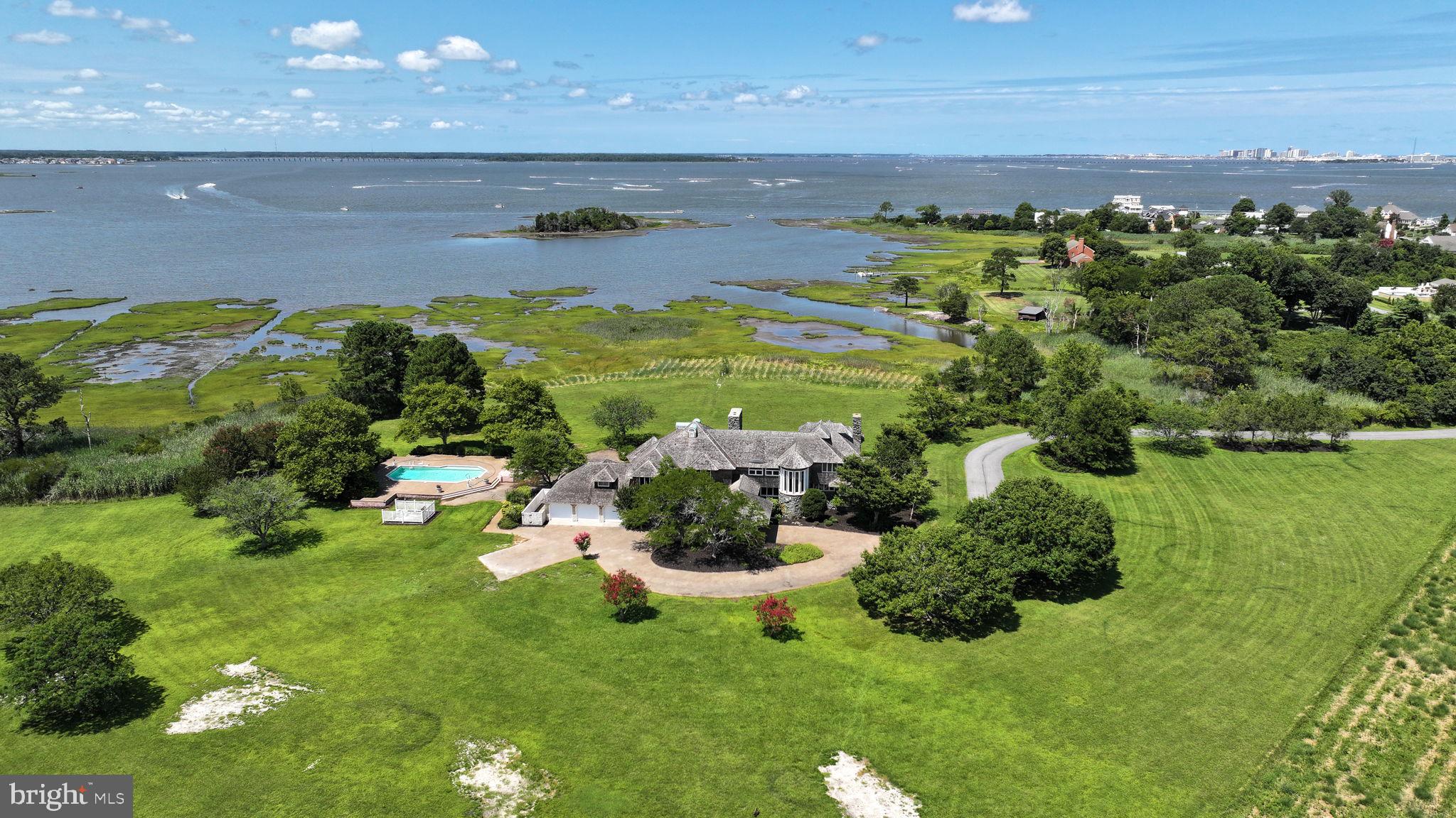 This 37-acre Waterfront Estate in the desirable West Ocean City Community of Captains Hill stands among Worcester County’s true legacy properties. A rare combination of Coastal Luxury, privacy, acreage and future opportunity. Set on a expansive rise overlooking the bay, the Estate commands sweeping water and skyline views that shift elegantly from sunrise to the golden glow of sunset. A long driveway leads you to the 8000+ Sq Ft Coastal Residence, a grand yet serene retreat surrounded by park-like grounds and mature landscape that creates an atmosphere of total privacy. The main Estate and grounds encompass 27 acres that feature a diverse landscape designed for both beauty and functionality. Such highlights include a 3-acre freshwater pond that anchors the properties tranquil setting, an outdoor pool with surrounding deck ideal for families and entertaining, an expansive lawn for gatherings and pets, a large covered porch perfect for enjoying the broad water views and nature, covered parking entrance and a three-car garage. The residence itself offers the architectural presence and scale expected of a Coastal Estate of this magnitude, with generous living spaces, impressive ceiling heights and endless potential for customization or enhancement. In addition, this Estate offers additional parcels and development potential that allows for flexibility for future use. Included in the offering is a 2.73-acre Waterfront Lot and 20 plated lots with their own road frontage. This rare land portfolio provides exceptional opportunities, ideal for a private compound, multi-generational retreat, curated development or long-term investment that makes this property uniquely valuable. Opportunities of this size, location and versatility rarely ever come to market. With commanding views, coastal proximity, and expansive acreage, this Captain’s Hill Estate stands as one of the region’s premier offerings, a property with both present-day grandeur and limitless future potential. A Coastal Treasure without equal.