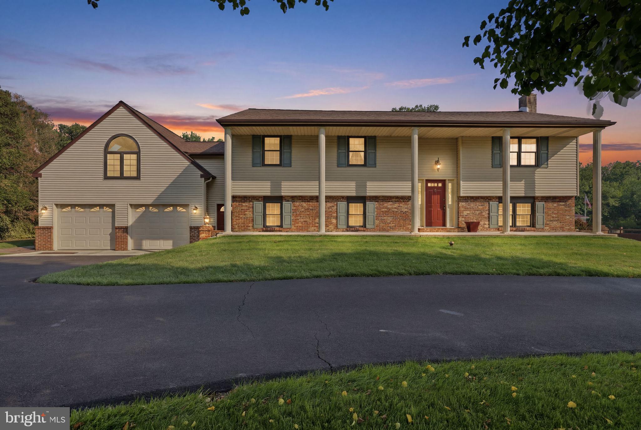 Welcome to 2733 Village Road in Langhorne, a versatile property offering spacious interior living areas, flexible bonus spaces, and generous outdoor grounds. The main residence features an inviting columned front porch, classic brick accents, and a wide paved driveway providing ample off-street parking that leads to an attached multi-car garage. Inside, the upper main level opens to a spacious living room with large windows that bring in abundant natural light. The updated kitchen features warm wood cabinetry with crown molding, an expansive breakfast bar island with stool seating, and an open connection to the dining area. The adjoining dining space is highlighted by hardwood flooring and a classic chandelier, creating a comfortable setting for everyday dining and entertaining. The upper level includes a spacious primary bedroom or flex suite with vaulted ceilings, a skylight, neutral carpeting, and an arched feature window. A notable feature of the home is the large bonus room with polished light wood floors, high ceilings with panel lighting, a separate exterior entrance, and oversized double wooden doors. This flexible area offers a range of potential uses, subject to buyer due diligence and any applicable zoning, permit, or municipal requirements. The property also includes a detached shed or workshop-style structure with coordinating siding, shutters, a gambrel roof, and its own entry door. The rear yard features an expansive lawn and an elevated deck with an integrated staircase, providing convenient access between the main living level and outdoor space. With its spacious layout, flexible interior areas, exterior structure, and generous grounds, 2733 Village Road presents a distinctive opportunity in Langhorne.