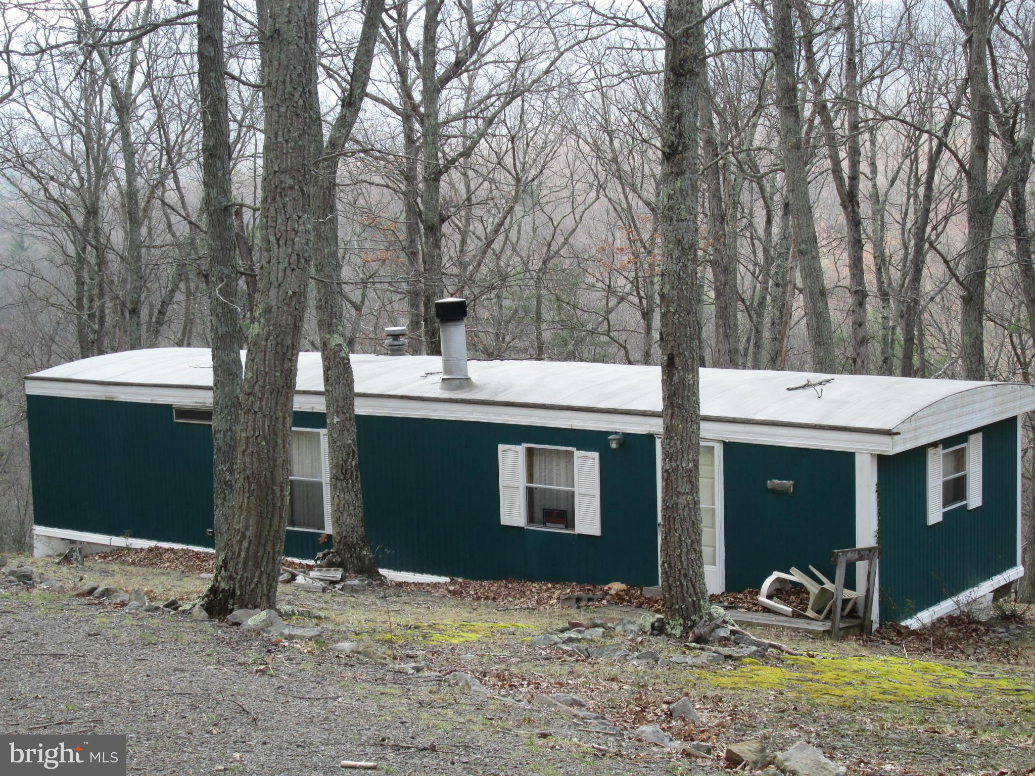 5 acre wooded lot with older mobile home, well, septic, & electric. Mobile is livable, has woodburning fireplace in living room, furnishings convey. Affordable weekend getaway or hunting cabin. Or live in the mobile while you build your dream home.