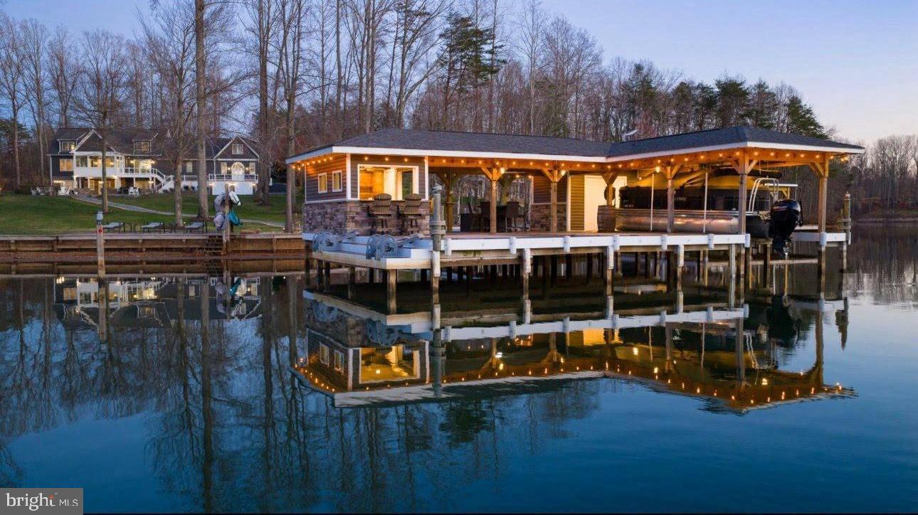 Extraordinary fully-furnished waterfront estate, perfectly set on the tranquil private side of Lake Anna, offering an unmatched blend of luxury, custom craftsmanship, and breathtaking natural beauty, along with high-speed fiber internet.  With 140+ feet of pristine shoreline and sweeping, unobstructed water views, this waterfront property presents a rare opportunity to experience a refined lake life.  Encompassing more than 5,600 square feet of thoughtfully designed living space, this home features seven generously proportioned bedrooms, including five private en-suite retreats, ensuring exceptional comfort and privacy.  Craftsman-inspired architecture is showcased throughout, highlighted by rich hardwood flooring, extensive custom trim work, chair rail, and other refined finishes.  The great room features soaring vaulted ceilings, custom built-in bookcases and shelving that frame an elegant fireplace crowned with a beautiful white mantle and stone work.  The large four-seasons room is encased by massive windows showcasing incredible views of the lake.  The expansive gourmet kitchen is designed for both entertaining and everyday living, featuring premium stainless steel appliances, a massive island graced by pendant lighting, a double wall oven, large gas cooktop, a built-in ice maker, beverage refrigerator, and an impressive walk-in pantry adorned with elaborate custom shelving.  The second floor offers two spacious primary suites, each with clear lake views, en suite bathrooms, and large walk-in closets.  The finished lower level further elevates the home’s entertaining capabilities with three additional bedrooms (one with a true functioning Murphy bed!), and a full-scale wet bar / kitchen with stainless appliances and custom stone work, creating an ideal space for gatherings and recreation.  Outdoors, the estate transforms into a private lakeside sanctuary set on a perfect flat lot showcasing incredible water views.  The custom-designed boathouse is a showpiece in itself, complete with a luxurious kitchenette, a vibrant tiki bar with roll-up windows, elegant granite countertops, a dedicated storage room, and a boat slip equipped with an electric lift. A sandy beach, a massive inviting hot tub, and expansive stone fire pit area with an abundance of outdoor furniture create the perfect setting for relaxation and unforgettable evenings along the water.  Adding both versatility and distinction, the property includes a completely finished attached garage with recessed lighting, built-in workspaces, cabinetry, and an extensive private primary suite above, offering exceptional space for guests, extended family, or creative use.  Surrounding the residence, meticulously curated landscaping and hardscaping wrap the property with breathtaking beauty, complementing the serene waterfront backdrop.  A 17-zone irrigation system keeps the landscaping fresh and hydrated.   Great location: close to groceries, restaurants, fast food, ABC, and more. This remarkable Lake Anna escape offers a rare convergence of elegance, privacy, and resort-style living, where every detail has been thoughtfully designed to deliver a truly exceptional waterfront lifestyle.  INVESTORS: short term rentals are permitted in this subdivision.  Lake Anna has been rated one of the top short term rental locations in the entire nation, and is home to some of the top-performing short term rentals in the Commonwealth of Virginia.  Purchase includes furniture, furnishings, decorations, appliances, and a significantly elevated lifestyle.