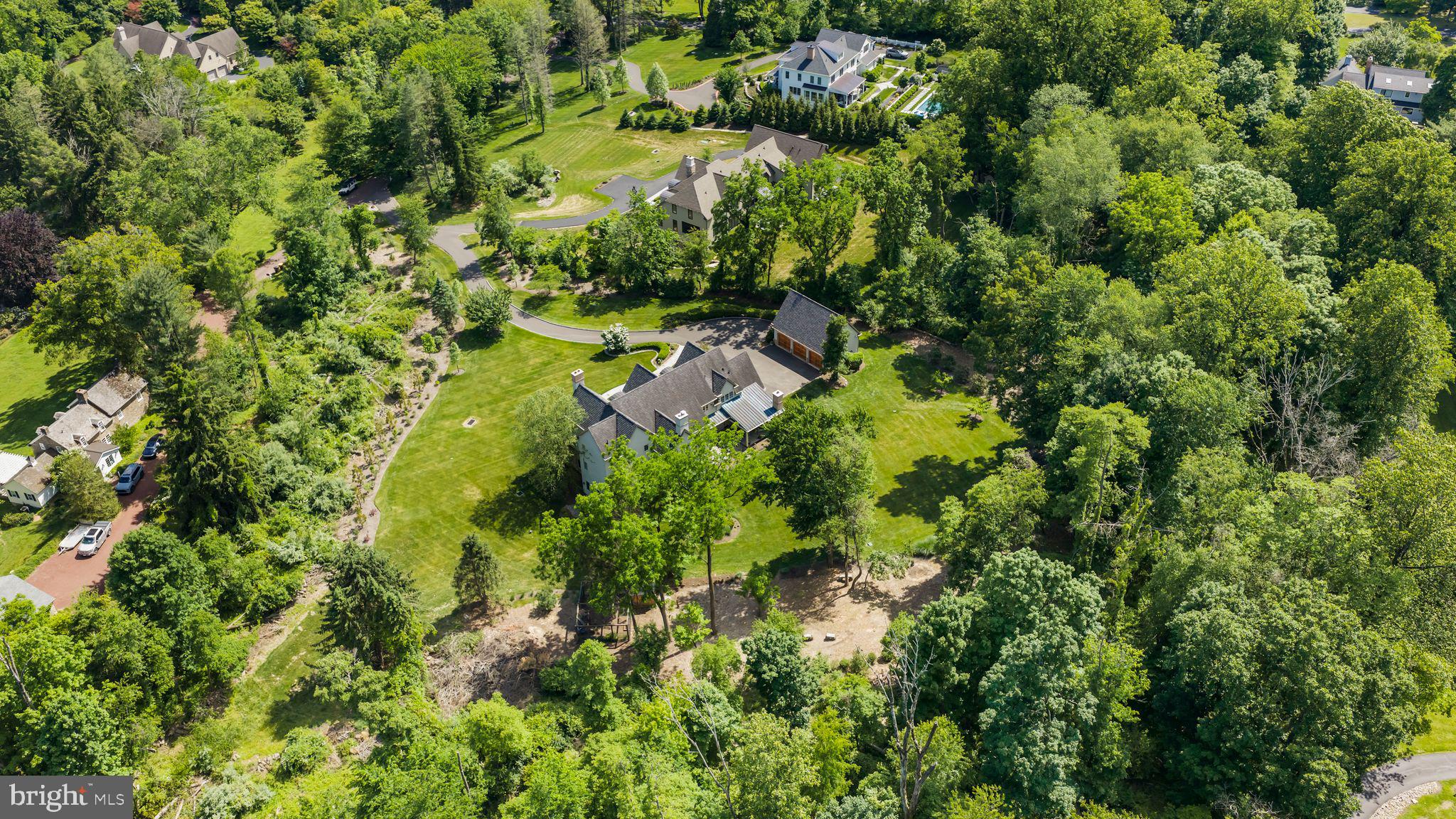 Tucked at the end of a private cul-de-sac within an intimate four-home enclave, this exceptional Zaveta-built custom estate is set on two beautifully landscaped acres just minutes from downtown Doylestown. Introduced by a winding Belgian block-lined driveway and surrounded by English garden-inspired grounds, the property blends architectural presence, sophisticated infrastructure, and refined craftsmanship across nearly 6,000 square feet of elevator-serviced living space. Built in 2015, the residence is defined by soaring ceilings, expansive windows, richly detailed interiors, and thoughtfully designed spaces that feel both elevated and exceptionally livable. A dramatic great room anchored by a floor-to-ceiling stone fireplace serves as the heart of the home, seamlessly connecting to a custom wet bar complete with wine storage, refrigerator drawers, and an ice maker. Nearby, the dining room transitions naturally into the updated gourmet kitchen, where quartzite countertops, paneled refrigeration, Thermador ovens, a concealed vent hood, and an oversized center island create an ideal setting for both entertaining and everyday living. Throughout the residence, upgraded Lutron lighting with high-CRI LED illumination, Sonos audio, four interior fireplaces, and extensive recessed lighting contribute to a warm yet contemporary atmosphere. The main level also features a spacious office with custom built-ins and a gas fireplace, along with a secondary gathering space offering flexibility for a media room, lounge, or additional entertaining area. A well-appointed mudroom and powder room are conveniently positioned nearby. The primary suite is privately situated on the main floor and offers a peaceful retreat with its own gas fireplace, generous walk-in closet, and a fully renovated Dolomite marble bath featuring radiant heated floors, a soaking tub, and an oversized walk-in shower. Upstairs, a second luxurious primary-style suite includes another spacious walk-in closet and marble bath with steam shower, while two additional bedrooms are thoughtfully arranged for family or guests. A uniquely designed fourth suite functions almost as its own private wing, complete with a sitting room, recreation or office space and powder room.
The walk-out lower level expands the home’s versatility with a spacious recreation room, private office, powder room, additional fireplace, and a fully equipped second wet bar with refrigerator, dishwasher, ice maker, and dual refrigerated drawers. Outdoors, multiple covered patios and gathering spaces overlook the impeccably maintained grounds, where mature trees and carefully curated landscaping create an exceptional sense of privacy. Additional features include full-property irrigation, 600-amp electric service, an attached three-car garage, a detached three-car garage ideal for collectors or hobbyists, and a recently installed invisible fence. Ideally located near the boutiques, dining, and cultural attractions of downtown Doylestown - and just a short drive from New Hope and the surrounding river towns - this remarkable property offers a rare combination of privacy, scale, luxury, and convenience in one of Bucks County’s most desirable settings.