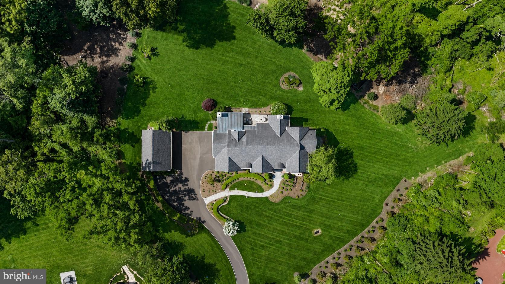 Tucked at the end of a private cul-de-sac within an intimate four-home enclave, this exceptional Zaveta-built custom estate is set on two beautifully landscaped acres just minutes from downtown Doylestown. Introduced by a winding Belgian block-lined driveway and surrounded by English garden-inspired grounds, the property blends architectural presence, sophisticated infrastructure, and refined craftsmanship across nearly 6,000 square feet of elevator-serviced living space. Built in 2015, the residence is defined by soaring ceilings, expansive windows, richly detailed interiors, and thoughtfully designed spaces that feel both elevated and exceptionally livable. A dramatic great room anchored by a floor-to-ceiling stone fireplace serves as the heart of the home, seamlessly connecting to a custom wet bar complete with wine storage, refrigerator drawers, and an ice maker. Nearby, the dining room transitions naturally into the updated gourmet kitchen, where quartzite countertops, paneled refrigeration, Thermador ovens, a concealed vent hood, and an oversized center island create an ideal setting for both entertaining and everyday living. Throughout the residence, upgraded Lutron lighting with high-CRI LED illumination, Sonos audio, four interior fireplaces, and extensive recessed lighting contribute to a warm yet contemporary atmosphere. The main level also features a spacious office with custom built-ins and a gas fireplace, along with a secondary gathering space offering flexibility for a media room, lounge, or additional entertaining area. A well-appointed mudroom and powder room are conveniently positioned nearby. The primary suite is privately situated on the main floor and offers a peaceful retreat with its own gas fireplace, generous walk-in closet, and a fully renovated Dolomite marble bath featuring radiant heated floors, a soaking tub, and an oversized walk-in shower. Upstairs, a second luxurious primary-style suite includes another spacious walk-in closet and marble bath with steam shower, while two additional bedrooms are thoughtfully arranged for family or guests. A uniquely designed fourth suite functions almost as its own private wing, complete with a sitting room, recreation or office space and powder room.
The walk-out lower level expands the home’s versatility with a spacious recreation room, private office, powder room, additional fireplace, and a fully equipped second wet bar with refrigerator, dishwasher, ice maker, and dual refrigerated drawers. Outdoors, multiple covered patios and gathering spaces overlook the impeccably maintained grounds, where mature trees and carefully curated landscaping create an exceptional sense of privacy. Additional features include full-property irrigation, 600-amp electric service, an attached three-car garage, a detached three-car garage ideal for collectors or hobbyists, and a recently installed invisible fence. Ideally located near the boutiques, dining, and cultural attractions of downtown Doylestown - and just a short drive from New Hope and the surrounding river towns - this remarkable property offers a rare combination of privacy, scale, luxury, and convenience in one of Bucks County’s most desirable settings.