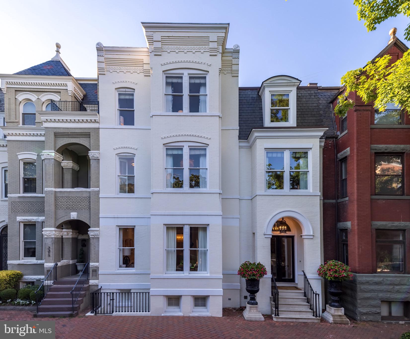 On a quiet, cobblestone block in historic Georgetown, stands a refined residence, fully renovated over several years by Smith Architectural Group. Meticulous thought went into every facet of this home. Original details are married with modern design elements so seamlessly that it feels as if they were always there. Upon entry, guests are offered views through the grand foyer to the reception rooms, a tranquil private garden, and an open well staircase. The formal living room boasts southern exposure and restored original windows with beveled glass. The stunning natural light extends through an opening to the dining room, which is illuminated by a Louis XV style, ormolu chandelier and gilt candle sconces in the evening, adding an opulent glow to dinner parties. Nesting doors separate the modern Bulthaup kitchen, perfectly designed for intimate gatherings or catered events alike. A series of French doors provide soft natural light, illuminating Caesarstone countertops extending the length of the twelve foot island, as well as along the perimeter. Informal seating gives guests front row seats to witness the home chef prepare picture perfect meals with a Gaggenau appliance suite, including integrated gas range and double ovens, that melds flawlessly with the modern aesthetic. Wine is perfectly chilled and at the ready in the dual zone wine fridge, whether enjoying the show in the kitchen or warming up by the fire in the informal living room beyond. When the weather is right, dine al fresco on the private wrap around terrace, featured in Gardens of Georgetown, by Edith Nalle Schafer, allowing the sound of the serene water feature to carry you away. As the evening draws to a close, a three story glass and steel installation by Graham Caldwell guides you upstairs, suspended below a skylight with the promise of a dance of light the next day. Entering the primary suite, one’s eye is drawn outside to a long balcony, then to the sumptuous bedroom, flanked by two ensuite bathrooms with walls clad in ethereal, reverse painted glass, and walk-in closets with bespoke organization systems. Each bathroom features a seamless glass enclosed shower, the larger of which boasts a Kohler steam shower for a true in-home spa experience whenever the mood strikes, while a separate soaking tub with adjacent TV offers a further venue for relaxation. An additional four hotel inspired bedroom suites occupy the remainder of the second and third floors. Overlooking the top of the staircase, where the Graham Caldwell installation “Ejecta” meets the sun, a spacious den is ideal for a home office or private getaway. Staff quarters, including full kitchen, full bath, and laundry facilities are located in the fully finished basement, with ample storage space. A secure, two-car garage opens to the alley behind this mini-estate in Georgetown.