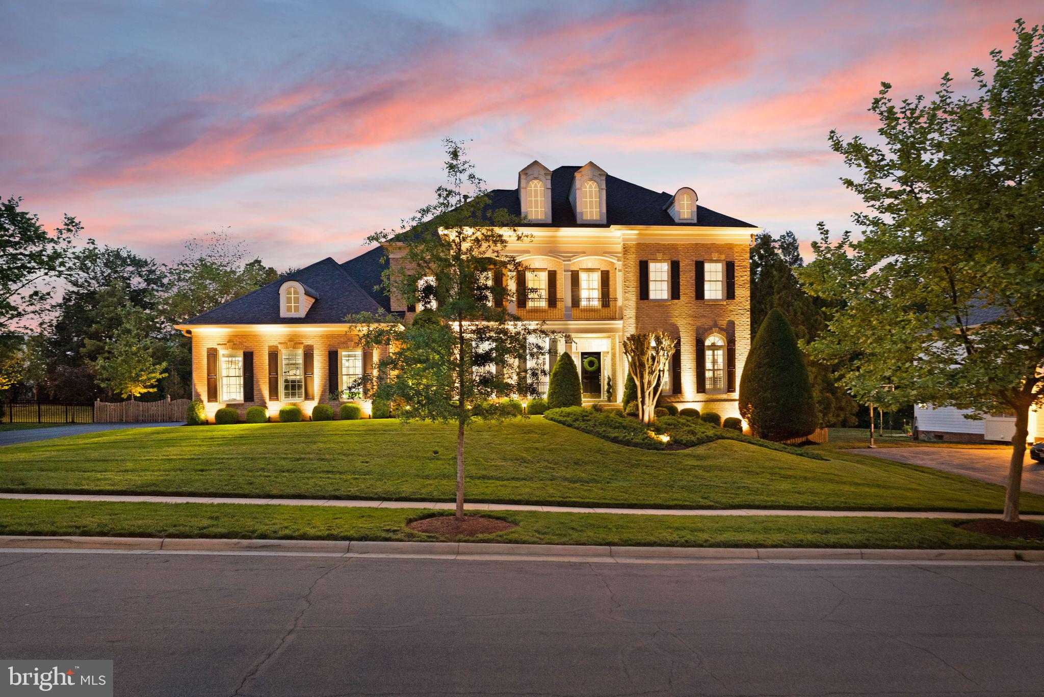 Ideally located on a premium lot backing to serene woodlands in Lansdowne on the Potomac’s exclusive West Goose Creek neighborhood, this Contemporary Colonial estate offers both exceptional luxury and resort-style living, complete with an incredible pool and spa pavilion and five private bedroom suites (750K in owner updates and improvements).  Arriving via tree-lined streets, the stately brick facade, landscaped grounds, covered front porch, and 3-car sideload garage welcome you into a home thoughtfully designed for both entertaining and everyday comfort. Inside, the foyer flows into formal living and dining rooms, each warmed by 10 sided gas fireplaces, built-ins, and contemporary lighting, with a private office nearby. A butler’s pantry with dual wine coolers transitions into the stunning, open-concept kitchen and family room. Suited to both large gatherings and casual meals, the kitchen boasts a grand center island beneath statement lighting, designer quartz counters and tile backsplash, extensive white cabinetry plus a walk-in pantry, and a high-end appliance suite including a GE Monogram refrigerator, Viking cooktop, and a new Bosch dishwasher in 2024. A spacious eat-in area and breakfast bar offer versatile dining options, while elegant archways lead into the family room, anchored by a double-sided fireplace connecting to a radiant, shuttered sunroom filled with natural light. A well-equipped mudroom and thoughtfully placed powder room complete this level. Outdoors, enjoy unparalleled resort-quality amenities with an impeccably upgraded backyard featuring a PebbleTec saltwater pool, spa, waterfall, and tanning ledge accented by LED lighting, auto pool-leveling, and a natural gas heater. Relax or entertain in the expansive 20’x26’ covered pool house, complete with a bar, full kitchen, bathroom, storage, dedicated HVAC, a built-in linear fireplace, and a 65” TV with speaker bar. Additional amenities include 3,000 sq ft of travertine decking, a wood-burning fire pit, an outdoor kitchen with grill and side burner, WiFi-controlled café lights, Sonos sound system, and professional landscaping with dedicated drainage. Upstairs, the luxurious primary suite offers a private retreat with a double-sided fireplace, sitting areas with coffee bar, three walk-in closets, A New marble-appointed bath featuring a freestanding tub, oversized shower, and treetop views. Three additional bedrooms on this level each have private full baths, including one with access to the large front balcony. The expansive walk-up lower level is designed for entertainment and flexible living, featuring a generous rec room with deluxe built-in bar, fireplace living area, half bath, a versatile bonus room, and a substantial storage room/workshop. The fifth bedroom suite with full bath and walk-in closet completes this level. Exterior walk-up stairs have the same Polyurea ‘better than epoxy’ floor covering as the garage, installed 2024 with lifetime guarantee. Garage features 3 separate stalls with extensive built-in storage and wall/ceiling racks. Among the many other noteworthy upgrades include new Carrier Infinity HVAC systems (2019), Owens Corning roof with transferable lifetime guarantee (2017), whole-house Ring security and fiber-based WiFi systems, extensive indoor and outdoor LED lighting, a 20-zone smart sprinkler system, plantation shutters, a dual sump pump, and a 75-gallon hot water heater (2023). Set within sought-after Lansdowne on the Potomac, residents enjoy exceptional community amenities including indoor/outdoor pools, fitness and business centers, playgrounds, sport courts, meeting spaces, and easy proximity to schools, Route 7, Lansdowne Town Center, Golf Club at Lansdowne, One Loudoun, hiking trails, and Elizabeth Mills Riverfront Park. Combining exceptional indoor elegance with an unmatched outdoor retreat, this meticulously upgraded home offers an extraordinary living experience in an ideal location. Welcome home.