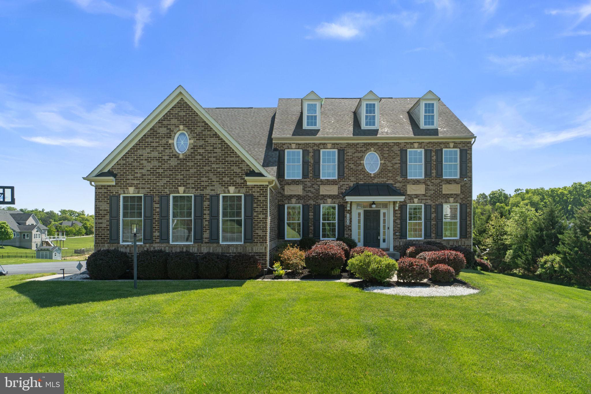 A stately traditional layout welcomes you with luxury vinyl tile flooring, elegant architectural columns, intricate crown molding, classic wainscoting, detailed ceilings, and custom wall cut-outs, all contributing to the home’s elevated design aesthetic across 5,602 finished square feet. // The well-appointed main level features formal living and dining rooms situated gracefully on either side of the foyer. The dining room is beautifully enhanced with lower wainscoting, a statement chandelier, and an elegant tray ceiling, creating the perfect atmosphere for intimate dinners and sophisticated gatherings. Just beyond, a breathtaking two-story family room serves as the heart of the home, highlighted by soaring coffered ceilings and a dramatic floor-to-ceiling stone-faced gas fireplace. // Seamlessly connected to the family room is the stunning gourmet eat-in kitchen, thoughtfully designed with both beauty and functionality in mind. Appointed with stainless steel appliances, granite countertops, a spacious center island, a walk-in pantry, custom mosaic tile backsplash, pendant and designer lighting, and a breakfast bar, the kitchen effortlessly flows into the inviting morning room. Bathed in natural light and offering panoramic views of the surrounding landscape, this tranquil space provides direct access to the expansive deck. The main level also includes a sophisticated private study with custom built-ins and French doors, a stylish powder room, and a functional laundry room conveniently located off the three-car garage featuring epoxy flooring. // The luxurious owner’s suite is a private sanctuary, complete with a tray ceiling, a serene sitting room with cathedral ceilings, and access to a secluded private balcony, dual walk-in closets, and a spa-inspired ensuite bath featuring a soaking tub, oversized separate shower, private water closet, and dual vanities. Three additional generously sized bedrooms and two full bathrooms complete the upper level, including a thoughtfully designed shared bath with dual access and a private ensuite bath for the third secondary bedroom. // The fully finished walk-out lower level offers exceptional versatility and comfort, featuring an expansive recreation room, a beautifully designed full bathroom with dual sinks and an oversized designer-tiled shower, a fifth bedroom with private walk-out access, and a sixth bedroom. A second laundry area is discreetly tucked away within a hidden closet for added convenience. Ideal for multigenerational living or extended guest stays, the lower level functions beautifully as a private in-law suite, complete with its own entrance and a full kitchen equipped with a cooktop, offering both independence and flexibility.