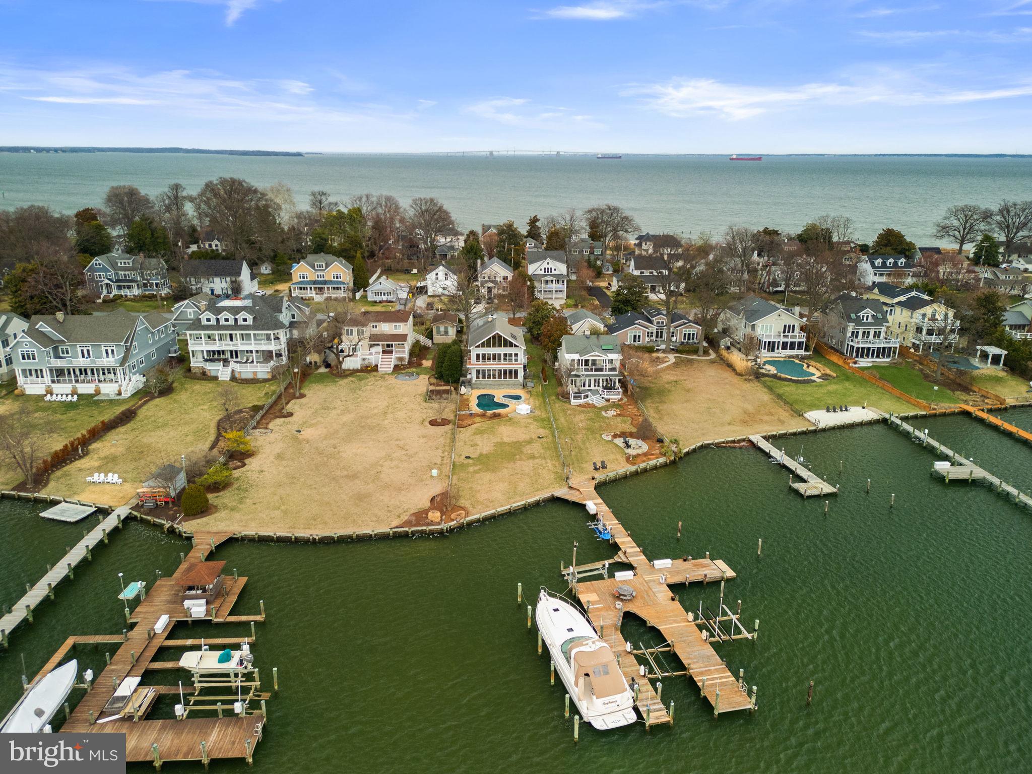 Welcome to 22 E Lake Drive! This exceptional waterfront residence offers striking architectural elements with expansive, light-filled interiors and seamless indoor-outdoor living along the Chesapeake Bay.
The main level open floor plan is designed for effortless flow and everyday living. The living room anchors the space, featuring a floor-to-ceiling stone fireplace and a wall of bi-fold glass doors that fully open to the pool and waterfront, creating a seamless extension of the home’s living and entertaining areas. Rich hardwood flooring, recessed lighting, and designer fixtures enhance the space throughout. A long, gallery-style entry hall offers a formal sense of arrival and includes a discreet powder room. The gourmet kitchen is both functional and elevated, featuring a large central island, custom cherry cabinetry, dark granite countertops, and a slate-tiled floor. High-end appliances include a gas range, double wall ovens, and a wine refrigerator. The slightly elevated, split-level design provides a clear vantage point over the dining and living areas while maintaining a defined culinary workspace.  
The home’s multi-level layout offers intentional separation of its four bedrooms for optimal privacy. The first upper level includes two well-sized bedrooms, a shared hall bath, and the expansive primary suite. 
The primary suite is a true sanctuary, defined by soaring wood-beam ceilings, a dramatic gabled roofline, and a wall of glass doors that open to a private balcony overlooking the water. A sliding barn door leads to the spa-inspired bath, wrapped in oversized charcoal slate tile and featuring an expansive wet room with multiple body jets and rainfall shower, a deep soaking tub positioned beneath a wall of windows, and a sleek floating dual vanity. The primary suite’s private balcony, finished with sleek cable railings, provides an elevated vantage point overlooking the pool, lawn, and panoramic water views. Above the suite, a unique loft space offers a quiet, sun-drenched retreat ideal for a home office, lounge, or library. Overlooking the bedroom below and framed by vaulted ceilings and a wide gable window, this elevated space captures sweeping waterfront views while maintaining a sense of privacy.  
A detached carriage-style garage includes a fully independent above-garage suite, offering exceptional versatility. This space features over 500 square feet of open living area with A-frame ceilings and large windows, a full bathroom, a modern kitchenette with quartz countertops and high-gloss cabinetry, and a dedicated laundry area. With its own private access, it is ideal for guests, an au pair suite, home office, or creative studio. 
The exterior is designed as a private waterfront retreat. A custom-shaped in-ground pool and elevated spa serve as the focal point of the backyard, surrounded by expansive decking for lounging and entertaining. A level, manicured lawn extends to the shoreline. 
Enjoy direct access to the Chesapeake Bay via a shared pier, perfect for boating, crabbing, or taking in the sunset. Unforgettable sunsets, a premier Bay Ridge Annapolis location, a short walk to the community beach, and quick access to Route 50 and Downtown—this is waterfront living at its finest. Schedule your private tour today!