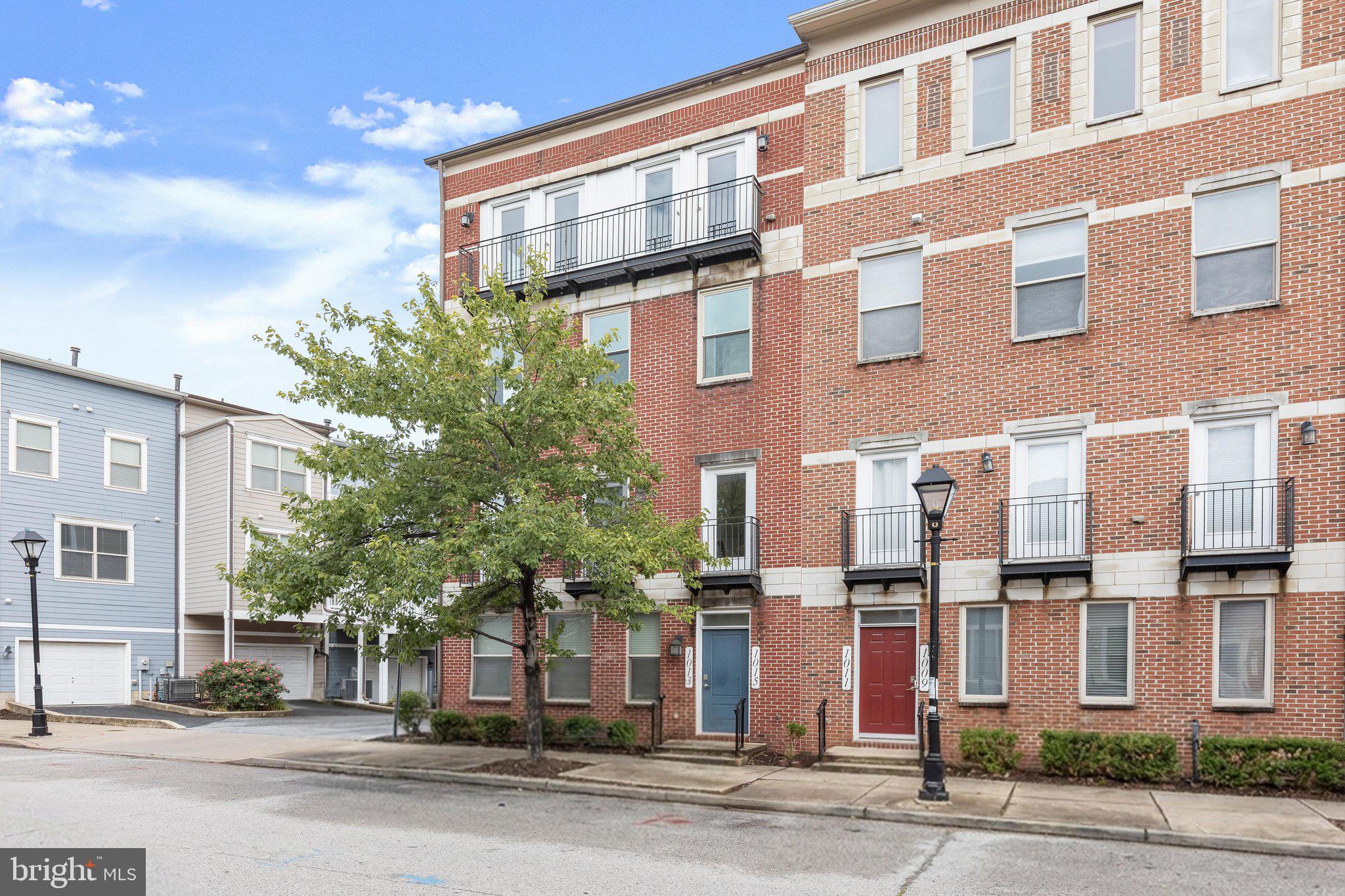 Contemporary finishes, soaring ceilings, and multiple private outdoor spaces distinguish this renovated condo townhome in the heart of Baltimore. Entry is through a shared vestibule with the neighboring unit, opening to a spacious interior with vinyl plank flooring throughout, nine-foot ceilings on the main level, and ten-foot ceilings upstairs. The interior has been freshly painted in a neutral color palette, creating a clean, cohesive backdrop throughout.
Crown molding adds detail to the spacious living room, which opens beyond a chair railing to the dining area. A modern brushed brass light fixture anchors the dining space and coordinates with fixtures in the adjoining kitchen and breakfast room. Sliding glass doors lead from the dining area to a private balcony, extending the living space outdoors.
White cabinetry, quartz countertops, stainless steel appliances, a pantry, and a classic subway tile backsplash complete the kitchen. The refrigerator, electric range, and microwave are all newly installed. A powder room finishes the main level.
Upstairs, the primary bedroom is framed by a wall of windows and opens to its own balcony overlooking the community and city. A walk-in closet and en-suite bath with a double-sink vanity, jetted soaking tub, and tiled shower create a well-appointed private suite. Two additional bedrooms feature vaulted ceilings and glass-paneled doors opening to the front balcony. They share a full bath with an upgraded vanity, while a laundry room adds everyday convenience on this level.
An attached one-car garage at the rear of the home provides secure parking and storage. Granby Street places you near Little Italy’s restaurants and cultural events, as well as the shopping, dining, entertainment, and waterfront promenade of Harbor East. The Inner Harbor, National Aquarium, Historic Ships, and waterfront activities are nearby, while Fells Point offers additional dining, nightlife, and historic character. Convenient access to I-83, I-95, public transit, and the Baltimore Water Taxi makes it easy to explore downtown and beyond.