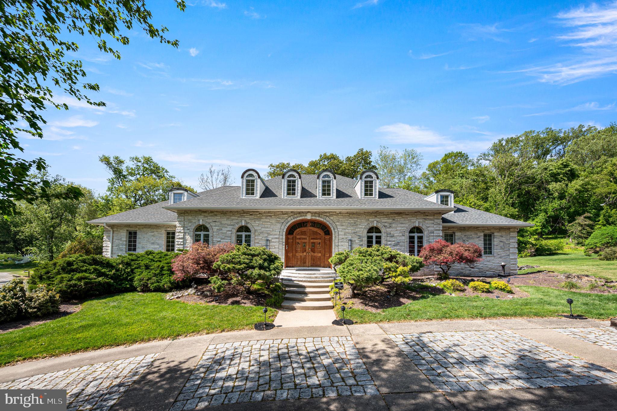 Welcome to 343 Wyndmoor Lane, where timeless European elegance meets modern refinement in sought-after Huntingdon Valley. This stunning 5-bedroom, 4.5 bath residence with a 2.5 car garage makes a striking first impression with its circular cobblestone driveway, hand-chiseled white Georgia marble exterior, arched windows, and grand double-carved entry doors. Step inside the dramatic foyer showcasing gorgeous onyx flooring, a Swarovski crystal chandelier, and a sweeping double curved staircase. Elegant formal spaces include a sunlit dining room with teak parquet floors and a sophisticated living room anchored by a marble and onyx fireplace. The kitchen features beamed ceilings, granite countertops, double ovens, a 48” Sub-Zero refrigerator, and a new KitchenAid cooktop, flowing seamlessly into a skylit sunroom and out to a breathtaking terrace overlooking professionally landscaped grounds with a pergola, waterfall, koi pond, and serene seating areas. The home continues to impress with a richly appointed study, spacious family room, and a luxurious primary suite complete with French doors opening to dual Juliet balconies, and a spa-like bath adorned with onyx finishes and Swarovski lighting. The fully finished lower level offers a true retreat with a Jacuzzi tub, steam room, sauna, fireplace, lounge, and entertainment space. Extensively updated for modern living, the home includes a new roof, new electrical system, new HVAC, new water heater, new washer and dryer, and new Raynor high-insulation garage doors and openers. Additional features include Pella windows, a built-in sound system, a central vacuum system, and a water filtration system. A rare blend of timeless craftsmanship and thoughtful upgrades, this exceptional residence offers a truly elevated living experience.