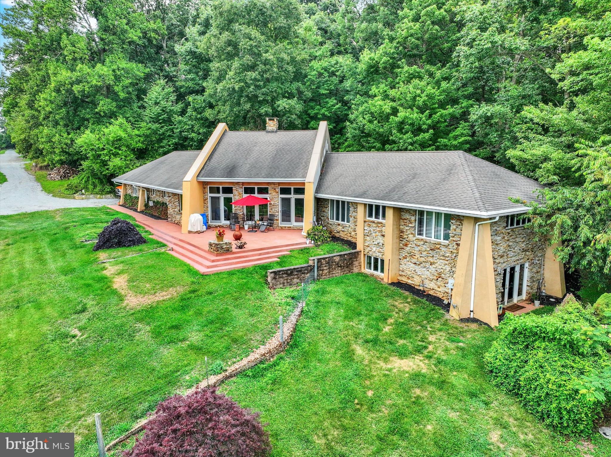 Priced BELOW Appraised Value!  Set on 25+ scenic acres in a peaceful, private setting, this one-of-a-kind property offers the perfect blend of distinctive architecture, comfortable living, and exceptional outdoor space. Designed with inspiration from Frank Lloyd Wright and incorporating passive solar principles, the home features concrete floors, extended roof overhangs, and abundant south-facing windows that invite natural light and connect the indoors with the surrounding landscape. The residence is thoughtfully designed for everyday living and entertaining. The expansive great room showcases vaulted, wood-beamed ceilings, dramatic walls of glass, and a striking floor-to-ceiling stone Russian stove that serves as a stunning focal point. The living and dining areas flow seamlessly into a recently updated (2025) kitchen featuring an island, pantry, and stainless steel appliances, with a conveniently located first-floor laundry room and powder room nearby. A private wing offers two spacious bedrooms, a cozy reading nook or ideal work-from-home space, and an updated (2023) full bath highlighted by a freestanding copper soaking tub. The finished walk-out lower level adds even more flexibility with a third bedroom or bonus room, an additional full bath, and a game room complete with a wet bar and access to a side patio. An attached 20’ x 23’ garage is currently used as a home gym but can easily be converted back to traditional garage space or additional living area. Outdoor living is where this property truly shines. Enjoy sweeping views, abundant wildlife, and a sense of tranquility that’s hard to find. A guest cabin provides a welcoming retreat for visitors or extended stays, featuring a covered front porch, cozy living area with woodstove and mini-split, full bath with walk-in shower, and a charming loft sleeping space. A winding trail meanders through the wooded portion of the property—perfect for exploring and enjoying nature. Additional outbuildings, including multiple large barns, offer incredible versatility for horses, hobbies, storage, workshops, or recreational use. Whether you envision a private retreat, a place to spread out and enjoy the outdoors, or a property with room to pursue your passions, the possibilities here are endless. Ideally located in a quiet country setting yet within a short drive to the PA/MD Line, to take advantage of Maryland hotspots. Outdoor enthusiasts will appreciate proximity to multiple state parks. A rare opportunity to own a truly special property where design, nature, and lifestyle come together seamlessly.  AGENTS-Please read Agent Remarks.
