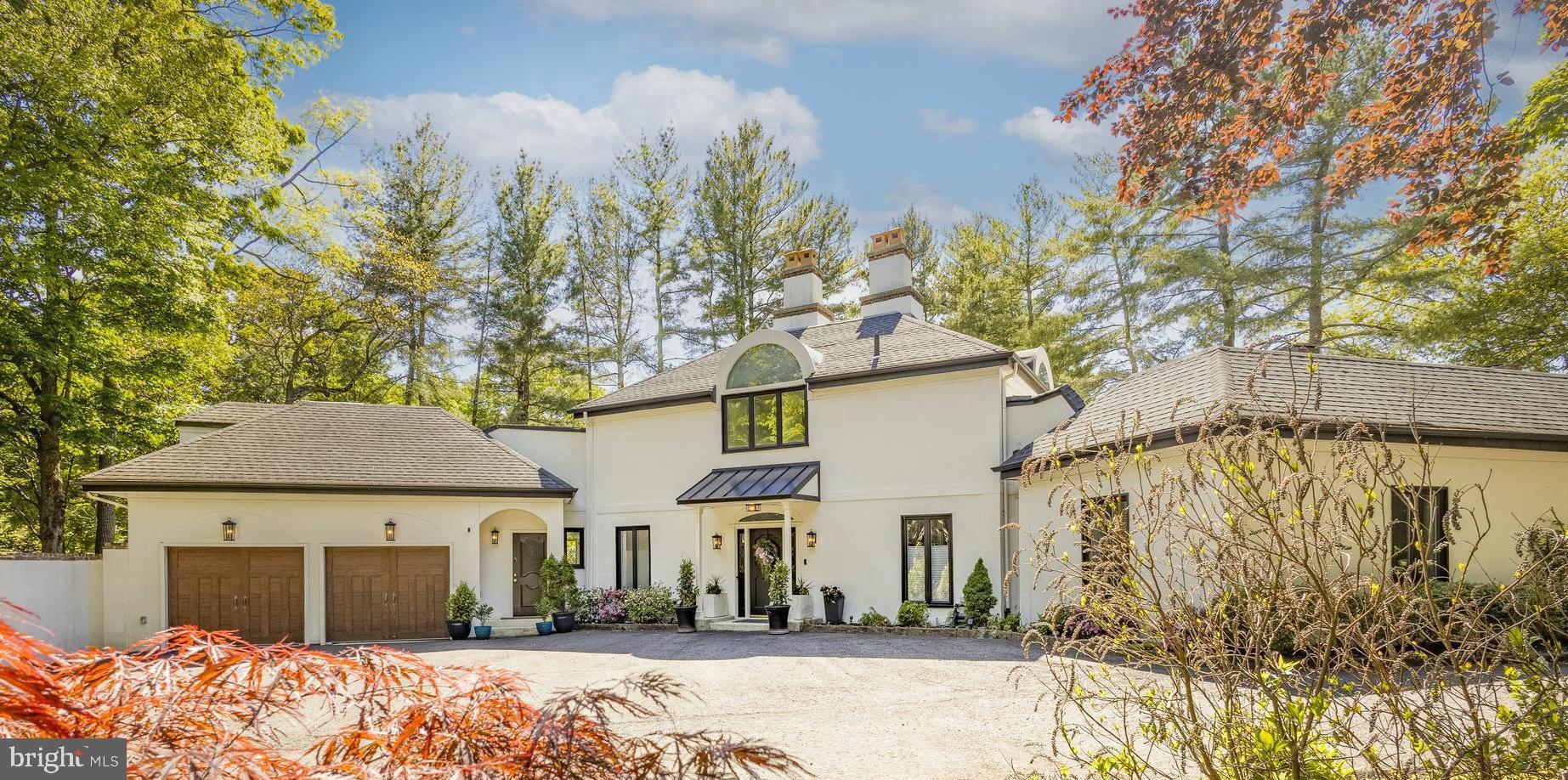 In the heart of Chestnut Hill, this exceptional European-inspired contemporary residence offers a rare blend of architectural living, organic warmth, and seamless connection to nature. Privately tucked behind a stately wall on nearly half an acre, the 5-bedroom, 5.1-bath home feels quietly removed from the everyday while remaining just moments from the Wissahickon, Germantown Avenue’s celebrated shops and restaurants, and convenient access to Center City. A gated driveway leads to a heated attached two-car garage with interior access, with infrastructure already in place for electric vehicle charging — reinforcing the home’s sense of privacy, comfort, and ease.
Beyond the bright, gallery-like entry, the eye is immediately drawn through the home toward its dramatic centerpiece: a spectacular glass conservatory rising at the rear of the residence like a private botanical pavilion. Flooded with natural light and framed by treetop views, the space blurs the line between indoors and out, anchored by a soaring antique chandelier and an oversized fountain repurposed as a sculptural planter. More than simply a sunroom, it is the architectural heart of the home — and the room you will inevitably find yourself gathering in.
Designed for both large-scale entertaining and intimate everyday living, the surrounding spaces balance modern luxury with warmth and texture. The living and dining rooms flow seamlessly into the conservatory, while a custom built-in wine and spirits cabinet reinforces the home’s effortless entertaining aesthetic.
At the center of the home, the warm contemporary kitchen combines clean lines, professional-grade appliances, skylit natural light, and understated functionality. Just beyond, a sunlit breakfast room or reading lounge with shelving opens onto a covered veranda overlooking the surrounding landscape and mature trees — an inviting setting for morning coffee, conversation, or quiet work-from-home moments.
A dramatic vaulted family room introduces a moodier counterpoint to the home’s airy entertaining spaces, pairing rich tones, oversized windows, a statement mantel, and integrated office alcove to create a comfortable lounge-like environment for relaxing or working from home. A nearby main-level laundry room adds everyday practicality.
Designed with comfort and privacy in mind, all five bedrooms feature ensuite baths. The main-level primary suite offers generous proportions and a calm, boutique hotel-inspired atmosphere. The ensuite bath features a soaking tub, oversized walk-in shower, single vanity, and clean contemporary finishes, while just beyond, the suite extends outdoors to a secluded walled courtyard with hot tub, private outdoor shower, and lounge area nestled beneath the trees.
The main family wing includes additional ensuite bedrooms with spacious closets and flexible accommodations for family or guests. Separate from this wing, two distinct upper-level suites are accessed by independent staircases, creating exceptional privacy and flexibility. One functions as a true second primary suite, complete with a lounge-style sitting area, spa-like bath, and private roof deck tucked among the treetops. The second upper-level suite offers ideal accommodations for guests, an au pair, multigenerational living, or the ultimate tucked-away hangout space.
The partially finished lower level provides flexible recreation, fitness, or lounge space, while a substantial unfinished area offers additional laundry area, extensive storage and utility space. Additional outdoor seating areas tucked throughout the property further enhance the home’s immersive connection to the surrounding landscape.
Ideally located just steps from Valley Green, St. Martins train station, and the boutiques and restaurants along Germantown Avenue, this architecturally curated residence is truly a home that must be experienced in person to fully appreciate the atmosphere, scale, and remarkable sense of escape it offers within one
