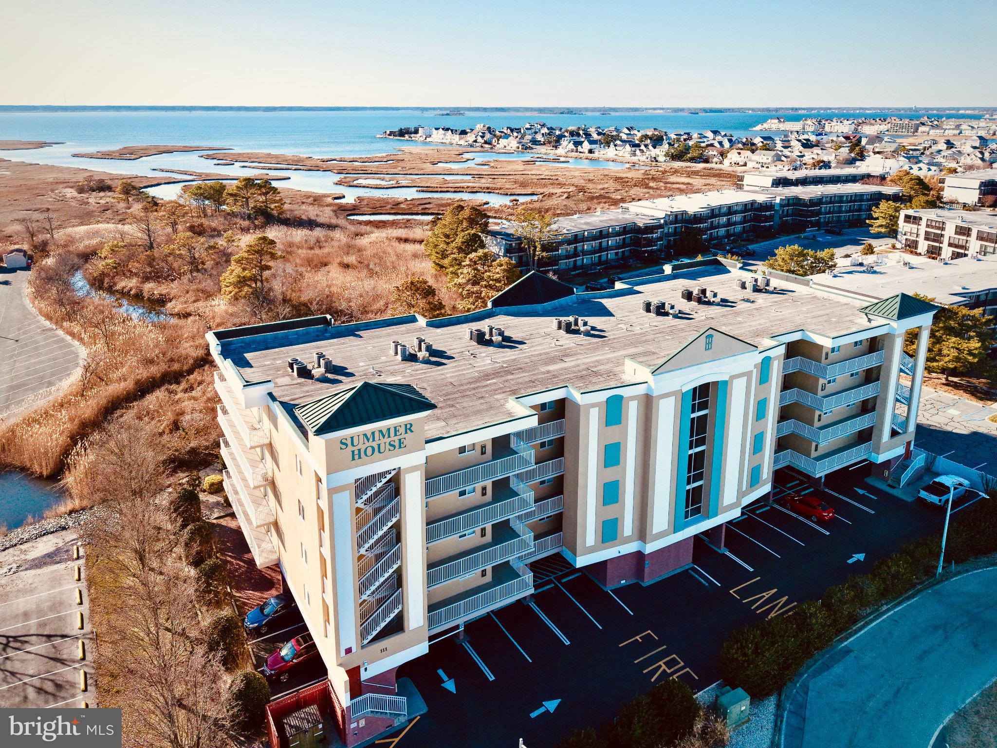 Welcome to Summer House, a well-appointed and secure condominium building in desirable North Ocean City, where coastal comfort meets relaxed seaside living. This beautifully maintained three-bedroom, two-bath residence offers a spacious, open layout, tasteful coastal finishes, in the heart of Ocean City. Inside, the home is finished in a neutral coastal color palette that enhances the abundant natural light and airy feel. High ceilings, crown molding, recessed lighting, and wide-plank luxury vinyl flooring can be found throughout the living spaces, creating an elevated beach aesthetic. The open-concept living area seamlessly blends the kitchen, dining, and family room, making the space perfect for both everyday living and relaxing. The family room features a cozy gas fireplace, perfect as endless summer days grow shorter, and a full wall of sliding glass doors that open to an oversized private balcony. From here, you can enjoy views of the community pool and glimpses of the bay, which become even more pronounced as the seasons change. The bright white kitchen is both stylish and functional, offering stainless steel appliances, a breakfast bar, generous cabinetry, and a pantry, all overlooking the dining and living areas. Just off the kitchen, a separate laundry room with a full-size washer and dryer adds everyday convenience. The primary suite is thoughtfully positioned for privacy away from the guest bedrooms. This spacious retreat includes a ceiling fan, walk-in closet, and a luxurious ensuite bath complete with a jetted soaking tub, separate stall shower, double vanity, linen closet, and private toilet room. Two additional guest bedrooms provide comfortable accommodation for family and friends and share a well-appointed hall bath. Summer House offers the ease of elevator access, and this unit includes two parking spaces, one of which is located in the covered under-building parking, as well as secure storge space for all of your beach gear! The residence is being sold furnished, making it move-in ready for immediate enjoyment. Residents and guests also enjoy access to the community pool, visible from the balcony, providing a relaxing spot to unwind after a day at the beach. Ideally located, Summer House places you just moments from the beach, iconic Ocean City attractions, popular nightlife, and an endless selection of outstanding dining and entertainment options. Whether you’re seeking a primary residence, vacation retreat, or investment opportunity, this inviting coastal condo offers the perfect blend of comfort, location, and beach life.