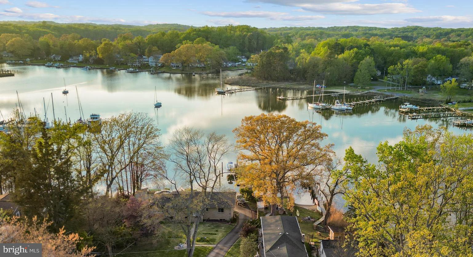 Welcome home! Nestled in this cherished waterfront community, serene views of Whitemarsh Creek greet you right from the front of the home. Whether you're looking to downsize into a low-maintenance water-oriented lifestyle or capitalize on incredible short-term rental potential, this property checks every box. This thoughtfully updated home offers an open floor plan ideal for effortless entertaining and everyday living, with rich hardwood floors and plantation shutters throughout. The generously sized living room features a charming brick corner fireplace and opens seamlessly into the gorgeously remodeled kitchen (2016), appointed with stainless steel appliances, an abundance of bright white cabinetry, granite countertops, and classic subway tile backsplash. The oversized island breakfast bar opens into the adjacent sunny dining area, where French doors lead directly to the wraparound deck for effortless indoor-outdoor living. A versatile flex space off the main living area is perfect for a home office, reading nook, or creative retreat. Both rare main level bedrooms feature elegant crown molding, plantation shutters, and ample closet space, connected by a beautifully updated jack & jill bath with a frameless glass door shower and modern finishes. The lower level offers a stunning full bath with an elegant freestanding soaking tub and floor-to-ceiling tile surround, dedicated laundry, and excellent potential for a workroom, hobby space, or additional storage. Step outside to the large wraparound composite Trex deck with remote-controlled retractable sunshade, where those front-facing water views set the perfect backdrop for sipping your morning coffee, dining al fresco, or simply unwinding as the sun sets over the creek. The fenced backyard is a true retreat as well, complete with a paver patio and brick fire pit ideal for gatherings. A storage shed and ample driveway parking large enough for parking an RV, boat, or summer guests round out the package. Major home system updates including roof (2022) with transferable lifetime warranty, HVAC (2024), water heater (2024), and windows (2015) offer true peace of mind. With Holiday Hill Marina only a block away, and both Weis Markets and Safeway conveniently within 5 miles, you'll be just minutes to charming downtown Annapolis, Mayo Beach Park, and Triton Nature Park. Quick access to Solomons Island Road, Central Avenue, Route 50, and Crain Highway. Come experience the relaxed water lifestyle this special community has to offer - schedule a private tour of your gorgeous new home today!