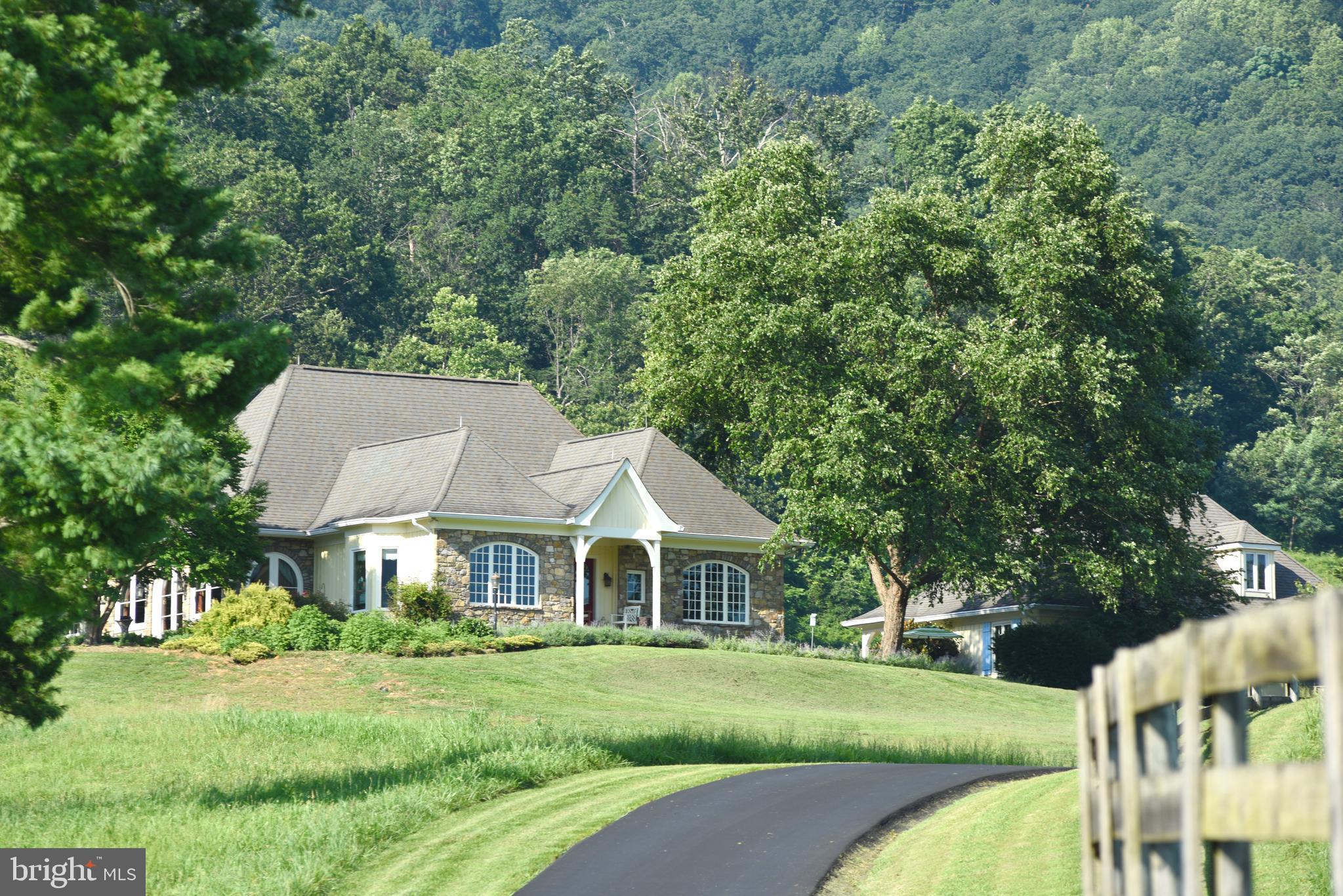 Imagine driving down a quiet country road past board fenced pastures, picturesque hayfields, old fieldstone walls and a local winery with the Blue Ridge Mountains on the horizon.  After about two miles of meandering through this idyllic country postcard, you wind to the top of a prominent knoll where MerryMead commands a breathtaking 360-degree view of the mountains, farms and forests of Gid Brown Hollow.

Rappahannock County is renowned for wonderful mountain views and all the Realtors extol the views of their listings.  But MerryMead is in a class by itself with perhaps the most breathtaking views of all.  The truly special views are difficult to describe, but you’ll know it when you see it.

The manor is country sophistication with a continental flair.  The steep rooflines, flared at the eves and front portico with arched double doors harken to a European villa.  The field stone and board and batten exterior solidly ground the home in Rappahannock County.  The western side of the house drinks in the panoramic views with a broad stone terrace, large, screened porch and wide pergola.  These delightful architectural elements are enhanced by lovely landscaping, expansive lawns and cool shade trees.

The 5,700 sq. ft. home offers spacious one-level living (although there are two guest bedrooms, each with its own bath upstairs), with the primary suite and an ensuite guest room on the main floor.

The simple portico opens to tiled entry hall with expansive open spaces beyond.  There is a large casual living room with fireplace, large west facing windows and glass doors that take advantage of the spectacular natural setting.  The high ceilings are enhanced by impressive curved and beveled beams.  Across a bar island and display cabinets is the formal dining room, large enough for full family gatherings.

The kitchen is open to the living and dining areas and has ample cherry cabinets, a large center island, granite counters, high quality appliances and a luminous Mexican tile floor.  Over the island is a whimsical light fixture fashioned from parts of an old Parisian elevator.  A convenient and sizeable pantry outfitted for food and cooking equipment is handily tucked behind the kitchen.  The kitchen area includes a pass-through to a cheerful, bright and airy casual dining area, with large windows, tall ceilings and Mexican tile floors.  This eating area opens to the screened porch and side terrace for east al fresco dining.

Adjacent to the kitchen is an expansive studio/craft room with running water.

The primary suite is at the far end of the house.  It includes a commodious yet cozy bedroom, sitting room, large soaking tub, walk-in shower, dressing room, separate toilet room and the Grand Canyon of closets.

Upstairs there are two ensuite guestrooms and there is a large unfinished basement.

Across an east facing stone terrace is an oversized three-bay garage, deep enough for ample workshop and storage spaces.  The grounds around the home, are beautifully landscaped with ornamental trees, shrubs and a profusion of flowering perennials.

The 21-acre property is open rolling hayfields and board fenced paddocks.  It includes a four-stall horse barn with water and electricity, paved driveway, stone gate entrance and an enormous amount of country charm.

 MerryMead  is located just 5 minutes from the charming villages of Washington, VA, and Sperryville, where you'll enjoy easy access to boutique shops and excellent restaurants. For larger shopping needs, Warrenton, Culpeper and Front Royal are conveniently located just 30 minutes away. This unique property combines the peacefulness and beauty of country living with proximity to vibrant local towns, making it a perfect retreat for those seeking comfort and convenience.