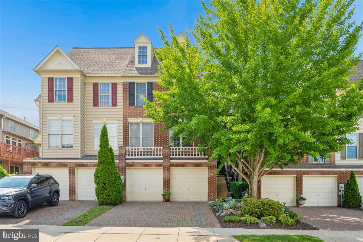 Meticulously maintained and beautifully presented, this picturesque townhome is nestled in one of Frederick’s most desirable communities, Wormans Mill, where residents enjoy a community pool, clubhouse, and true low-maintenance living with lawn care included. An added bonus of this neighborhood is the walkability to restaurants, shops, and everyday conveniences just moments from your front door.
From the moment you arrive, the paved driveway and distinctive two-car garage create a striking first impression. Inside, you'll immediately notice how exceptionally well cared for this home has been. Fresh paint throughout provides a clean, updated feel, while beautiful hardwood flooring spans the main living level and adds warmth and character to the space. The entry level offers exceptional flexibility. The main lower-level living area is ideal for a recreation room, home gym, media room, or guest space, while a separate den provides the perfect option for a home office, hobby room, or a fourth bedroom The main living level is filled with natural light thanks to an abundance of windows that showcase the rich hardwood floors and inviting layout. The thoughtfully designed kitchen has been impeccably maintained and serves as the heart of the home. A unique three-way fireplace between the kitchen and family room provides both warmth and architectural character, creating distinct spaces while maintaining an open and inviting flow Step outside from the kitchen onto the rear deck overlooking what can only be described as a private garden oasis. The beautifully landscaped backyard features an elegant paver patio, carefully curated plantings, and years of attentive care. Two mature crepe myrtle trees provide seasonal color and shade, creating a peaceful retreat perfect for relaxing, gardening, or entertaining guests. Beyond the patio, you'll enjoy views of a spacious grassy common area surrounded by mature trees, all maintained by the HOA, offering added privacy and a serene park-like backdrop. Upstairs, the home features three bedrooms and two full bathrooms. The spacious primary suite boasts vaulted ceilings, his-and-her closets, and a beautifully remodeled bathroom complete with double vanities, a soaking tub, and a separate shower. Above the primary suite, a loft provides the perfect space for a home office, reading nook, workout area, or private retreat.