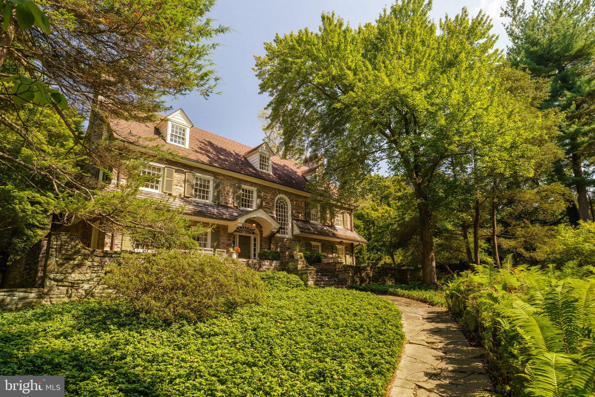 Welcome to this grand early 20th-century Colonial estate—an exceptional offering on one of West Mount Airy’s most coveted park blocks. Set on nearly an acre and bordering the Wissahickon, the home combines timeless stone architecture with thoughtful renovations by a noted architect, Addison H. Savery, showcasing custom detailing throughout.Behind the tree-lined frontage, privacy and serenity unfold with stone terraces, mature gardens, and a sparkling saltwater pool—all just minutes from the shops and restaurants of both West Mount Airy and Chestnut Hill. Inside, three levels (plus basement) offer over 5,000 square feet of living space with five bedrooms, five full baths, and a powder room. The gracious entry foyer with its curved staircase sets the tone, leading to a formal living room and dining room—each anchored by Mercer tile fireplaces. A sun-filled gourmet kitchen opens to a glass-wrapped sunroom with new French doors, alongside a den, mudroom, and powder room. The second floor hosts three en-suite bedrooms, a bonus room, a laundry room, and an additional full bath. The third floor offers versatility: a guest apartment or family retreat with two bedrooms, a living area, office, and full bath. Additional highlights include a full unfinished basement and a two-car garage. This is a home that balances classic grandeur with modern livability—a private retreat on the Wissahickon, yet seamlessly connected to all the best of Philadelphia.