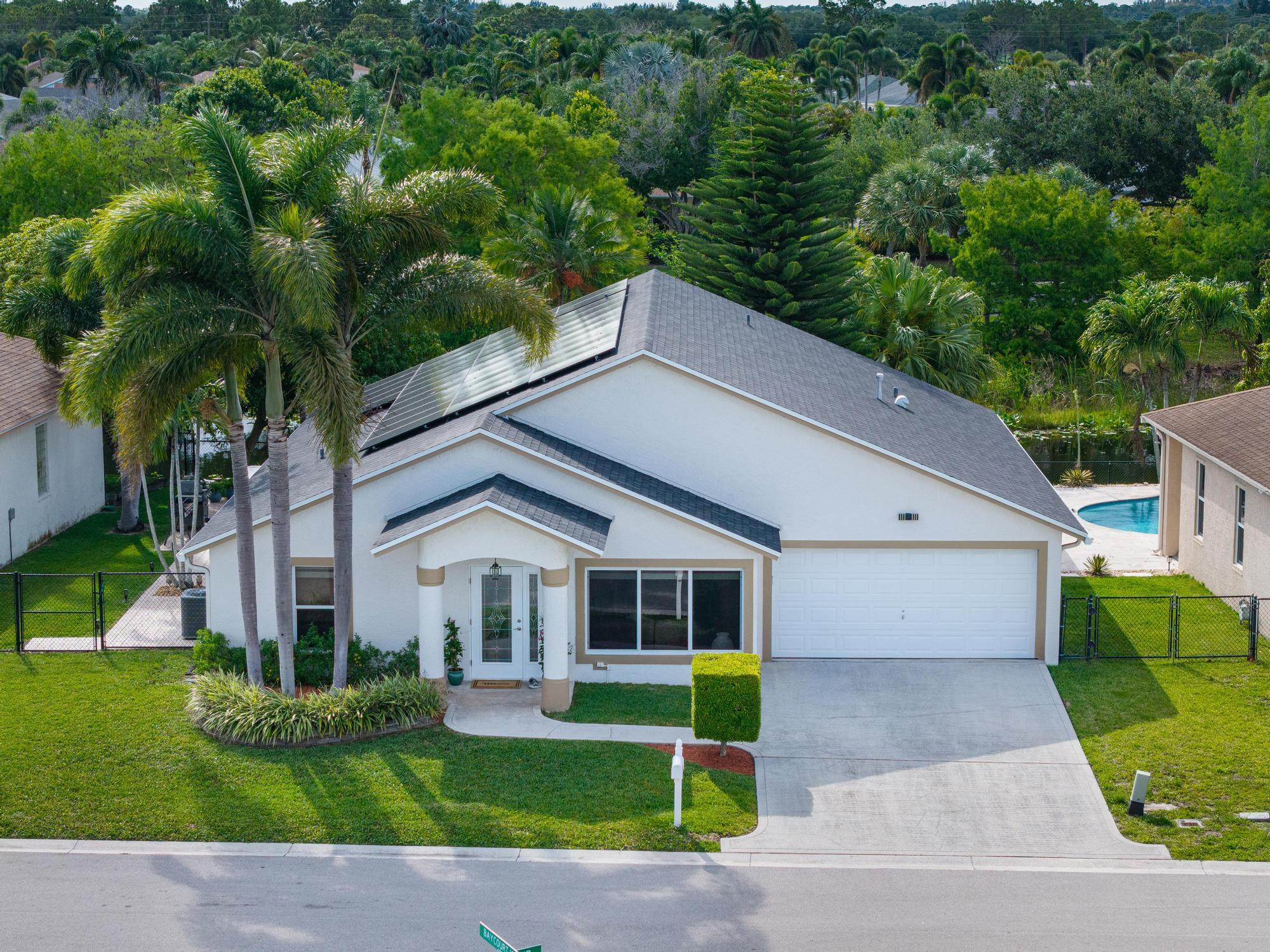 Set along a premier waterfront with approximately 67 feet of frontage, this exceptional one-story upgraded home delivers the rare combination buyers crave: privacy, serenity, and everyday convenience. With no homes directly in front or behind, gentle breezes sweep across the water and the backyard becomes your personal retreat. The hard to find 4 bedroom, 2 bath layout balances comfort and functionality under soaring cathedral ceilings with natural light and tranquil waterfront views. Enjoy an upgraded kitchen and bathrooms featuring natural stone tile, granite, warm wood cabinetry, and frameless glass showers. Major improvements include a 2024 roof, 2024 Carrier HVAC, 2024 solar panels, 2023 impact windows, a 2023 gas water heater, and an outdoor Jacuzzi for effortless waterfront living. The primary suite is a standout, offering direct access to the porch and patio for effortless indoor-outdoor living, plus the convenience of stepping straight from the primary bath into your outdoor oasis. The open kitchen is ideal for entertaining, featuring abundant natural light, a picturesque window overlooking the lake, and large sliding glass doors that keep conversations flowing from indoors to out. Ceramic tile runs throughout the home for clean, cohesive living, and the flexible stove setup accommodates either gas or electric. Out back, unwind in the outdoor jacuzzi, enjoy the shade and beauty of fruit trees, and savor the peaceful lake views that make this home feel like a private getaway with space to built your own pool. Approximately 1,045 sq ft of Stonehurst modular stone units enhance the rear and left side of the residence, adding character, texture, and curb appeal. Solar panels elevate energy efficiency, and a rare 6 foot high attic provides unusually spacious, walk-in-style storage. Every carefully selected item below conveys with the property in full working order move in ready from day one. Outdoor: jacuzzi, gazebo, outdoor stove, storage shed, lawnmower, and lawn trimmer. Interior: Sharp 28" TV (garage), LG 50" TV (primary bedroom), Philips 51" TV (bedroom 3), Samsung 38" TV (bedroom 1), seven ceiling fans, dining room chandelier, two wood desks, full-size garage refrigerator, red lipstick woman glass wall art, and wine glass wall art.   A truly turnkey opportunity, simply arrive and begin living. Perfectly positioned for daily convenience and easy commuting, with quick access to Forest Hill Blvd, Jog Road, Florida's Turnpike, and I-95. Ideally located approximately 15 minutes from Palm Beach International Airport and 20 minutes from the beach.  Enjoy quick access to top shopping and essentials, including Publix, Walmart, and Target just a few minutes away, plus The Mall at Wellington Green for dining and retail, City Place and Palm Beach Outlets for even more shopping, entertainment, and nightlife options. Whether you are commuting, traveling, or heading out for a weekend on the water, you will love being just about 15 minutes to Palm Beach International Airport, roughly 20 minutes to Lake Worth Beach, and approximately 25 to 30 minutes to Palm Beach. This is more than a home, it is a peaceful lakefront sanctuary designed to be enjoyed every day.