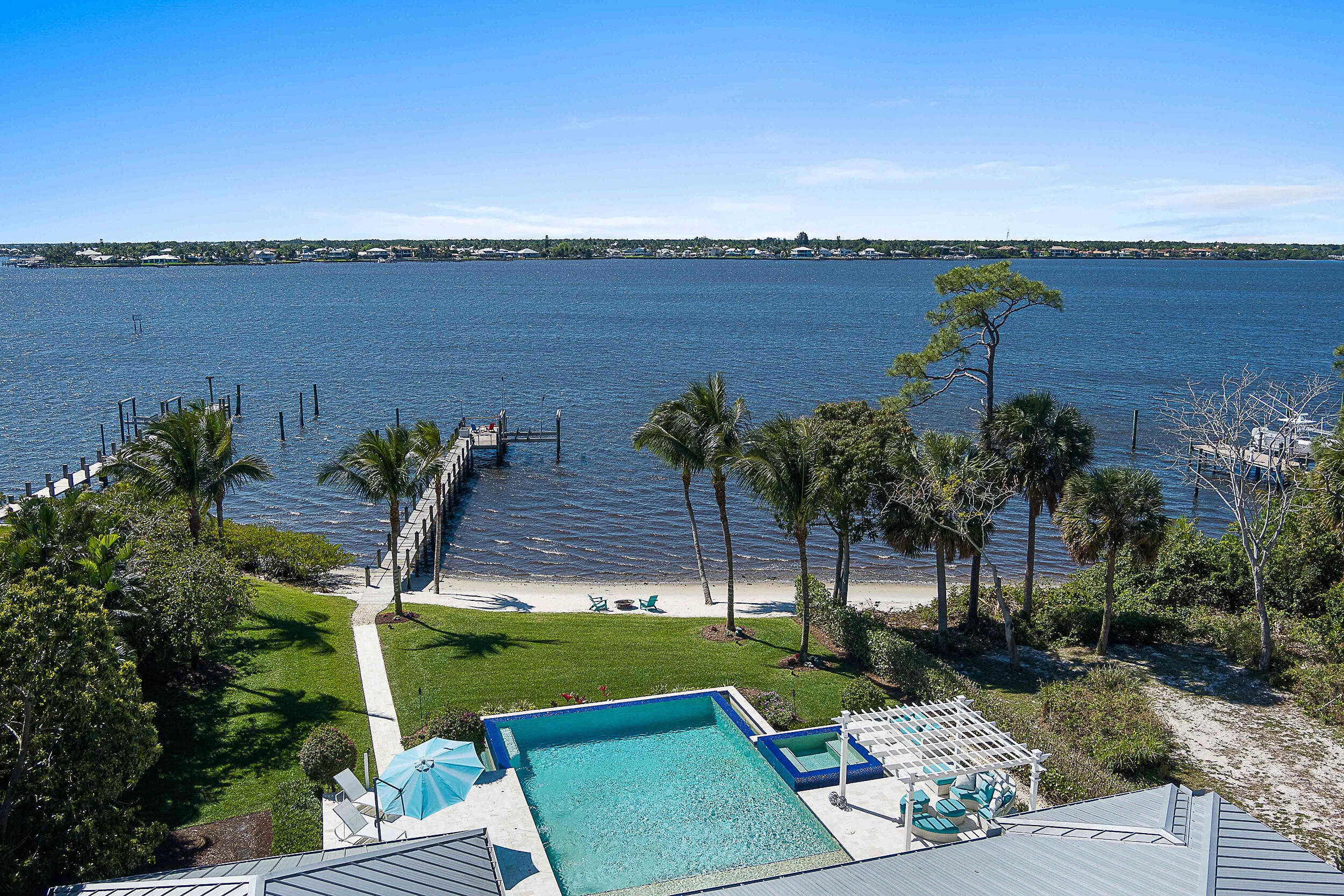 Accepting all offers.  Enjoy waterfront living in this 2017 custom estate, now offered at a new reduced price. Privately set behind gates on nearly an acre, the residence was designed to capture sweeping views of the St. Lucie River while blending comfort, elegance, and sophistication.Inside, you'll find six spacious bedrooms, two private offices, 4.5 baths, a 4.5-car garage, & a versatile guest or in-law suite. Soaring ceilings, a sleek metal roof, and seamless indoor-outdoor flow showcase Florida's signature style.Enjoy resort-level living with a spectacular infinity-edge saltwater pool, spa, sun shelf, fully equipped summer kitchen, generator, and your own private sandy beach. Nearly 115 feet of pristine waterfront with a deep-water dock and 20,000-pound lift accommodates ya up to 70 feetbringing world-class boating right to your doorstep.
Lush tropical landscaping ensures privacy and a serene retreat, making every day feel like a getaway. With its recent price adjustment, this estate represents an exceptional opportunity to secure the pinnacle of waterfront living.