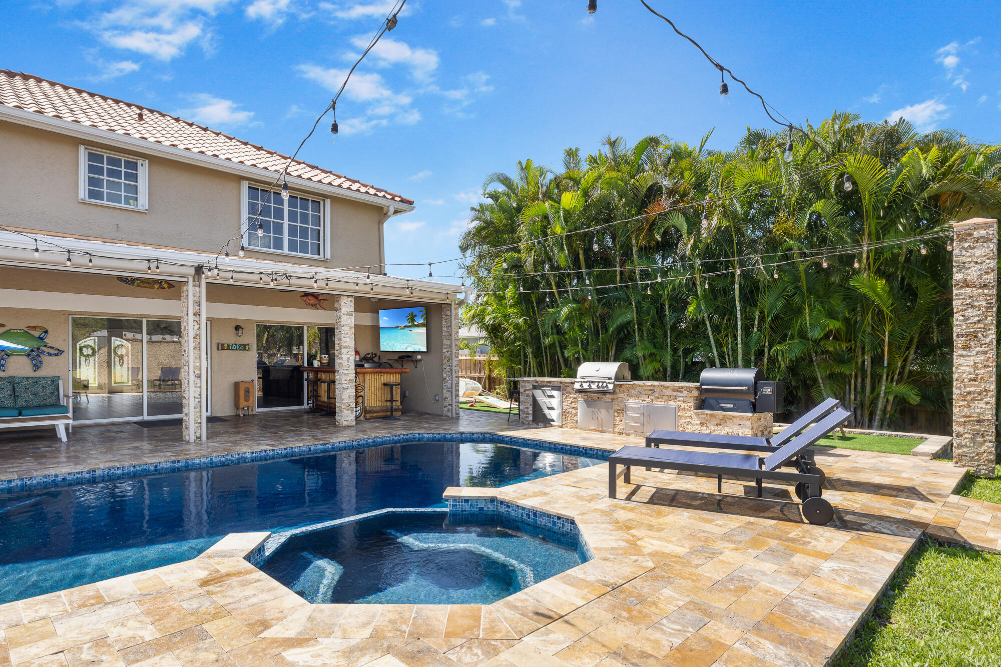 This Ocean-access waterfront estate is set along the St. Lucie River and features 4-bedroom, 3-bathroom, 2-car garage, and covered parking for a Boats or an RV. The 1st floor game room and cabana bath can also function as a 5th bedroom and first-floor ensuite. The kitchen was tastefully updated with quartz countertops and a new Bosch refrigerator, opening into an oversized living space finished with luxury LVP flooring throughout the main level. Upstairs, you'll find two guest bedrooms and an expansive primary suite complete with a walk-in closet, soaking tub, seamless glass shower, and dual vanities. The two car garage houses laundry and is air conditioned through a minisplit unit. The backyard is a true showpiece. A travertine patio surrounds the renovated saltwater pool and spa, featuring a sun shelf, Jewelscape finish, automated equipment, and gas powered heater. The screened-in porch is equipped with retractable, hurricane-rated screens, allowing you to fully enclose the space at the touch of a button. Designed for both relaxation and entertaining, the outdoor space includes a fully turfed yard with commercial-grade playground equipment, along with a custom outdoor kitchen featuring a gas grill, smoker, extended bar seating, and dedicated a game area. At the water's edge, the dock has been upgraded with a 20x40 extension and a tiki hut complete with lighting, TV, and Sonos surround sound. A 9,000 lb boat lift makes getting on the water effortless, with ocean access in approximately 30 minutes. Additional exterior upgrades include a concrete seawall, automatic irrigation system, and security trim lighting. The home is equipped with a Tesla charging station, whole-home generator, and a 50-amp RV hookup, supported by two buried LP tanks.  Located just minutes from The Port District, a growing waterfront destination featuring restaurants, cafés, marina access, and entertainment, this home offers both privacy and proximity to one of the area's most exciting developments.