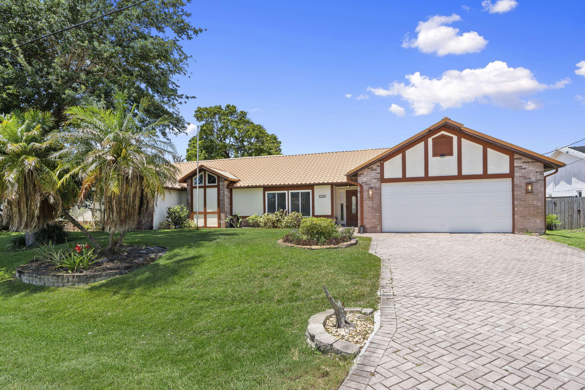 Set on an oversized double lot with direct canal and ocean access, this 4-bedroom, 3-bath home delivers 2,912 square feet plus an attached private suite complete with its own bedroom, full bathroom, kitchenette, office, private entrance, and dedicated garage. Inside the main residence, the kitchen has been completely updated, white shaker cabinets, granite countertops, an expansive center island with ample seating, stainless appliances, and wine cooler. The layout flows seamlessly into two separate living areas and a dedicated dining space with vaulted ceilings and crown molding throughout. The primary suite has direct pool access and an en suite that earns the word spa: dual vanities, rich walnut cabinetry, granite counters, round mirrors, water closet, and a large frameless glass walk-in shower with designer tile detail. Out back, enjoy a large screened lanai with salt water pool, full summer kitchen, and covered lounge area. The canal frontage extends to a private dock with power, currently setup for a 14ft boat, and covered gazebo. Additional highlights include solar panels (owned), hurricane-impact windows and doors throughout, whole-home reverse osmosis water filtration, central vacuum, metal roof, a fully equipped private cedar sauna, and a paver driveway surrounded by mature tropical landscaping. The Tudor-accented facade and lush canopy give the front of this home striking curb appeal that immediately stands out. Canal access. Double lot. Private in-law suite. Sauna. Saltwater pool. A property designed to offer both luxury and versatility.