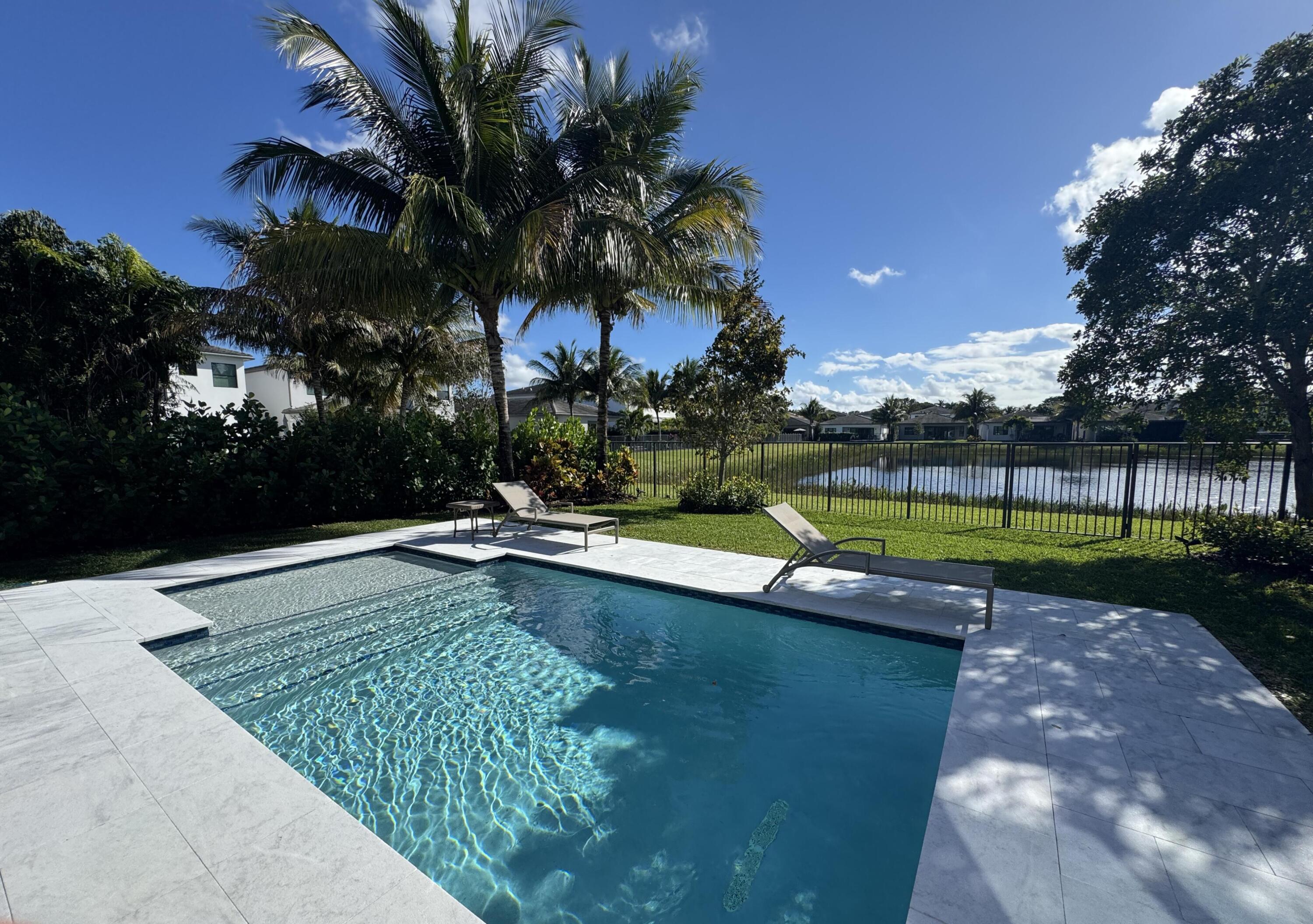 Upgraded Tahiti Expanded model on a premium lake lot in the sought after Lotus community. Upon entering, soaring vaulted ceilings, 8 inch moldings, and expansive 24 x 48 Italian porcelain tile floors define the main living areas. The expanded open concept great room creates a spacious and inviting atmosphere. The kitchen features brand new porcelain countertops and backsplash with sleek modern finishes. The primary suite serves as a private retreat with French doors leading to the covered patio. Two additional bedrooms allow for versatile use, and the remodeled garage includes vinyl flooring. Enjoy fully fenced outdoor living with a modern pool, expansive travertine patio, outdoor shower, kitchenette, lush privacy landscaping, and tranquil lake views.