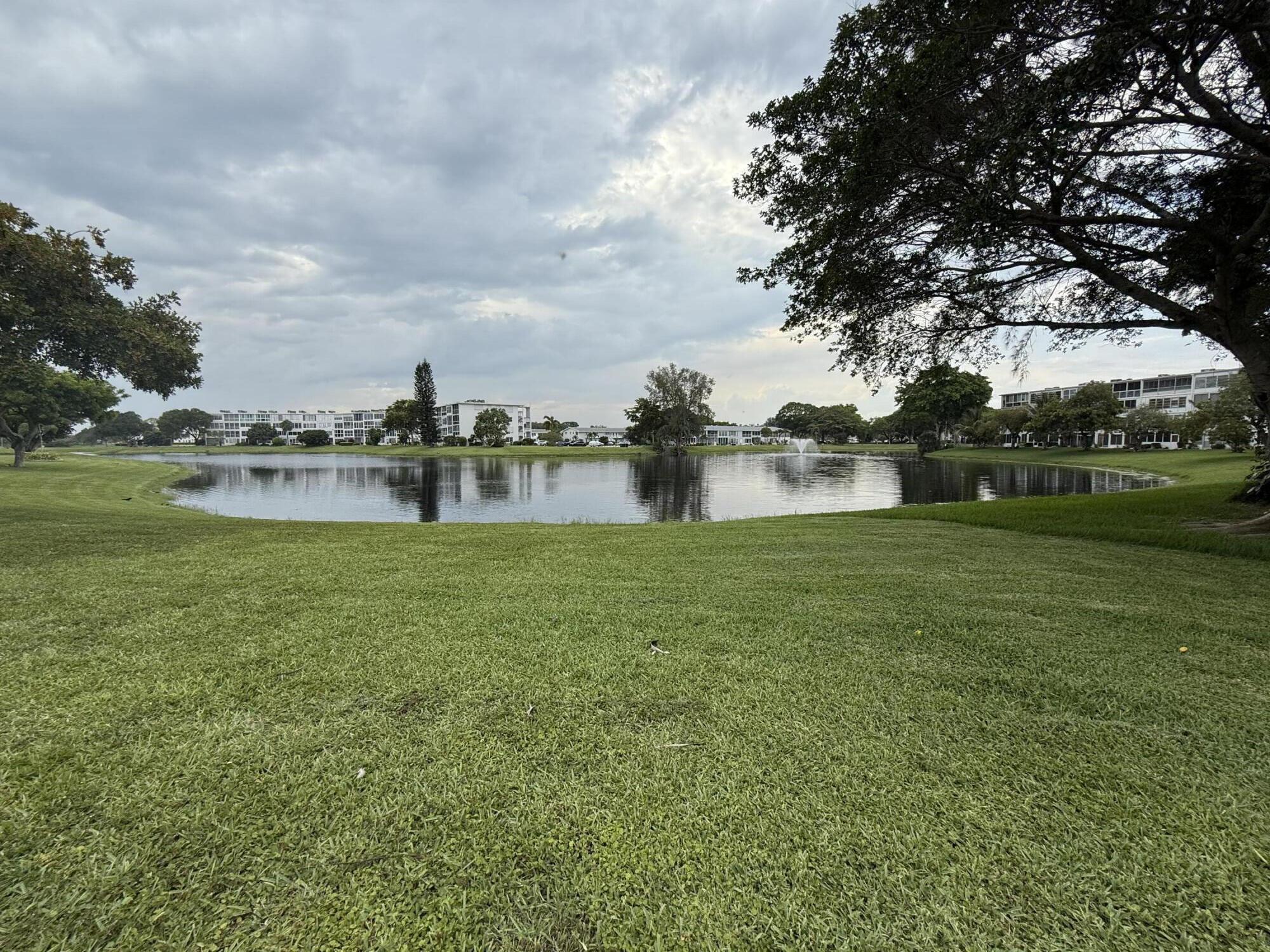 Welcome to Century Village, an active 55+ gated community. This bright, top-floor corner location offers South Florida living at its best with 2 bedrooms, 2 bathrooms, and 983 square feet of living space. The kitchen features wood cabinetry and ample storage, with tile flooring throughout the kitchen and living areas and carpet in the bedrooms. The spacious primary suite includes a custom walk-in closet. Relax or entertain on the enclosed private patio while enjoying stunning panoramic water views and excellent natural light throughout the home. Conveniently located just minutes from shopping, restaurants, and the beach.