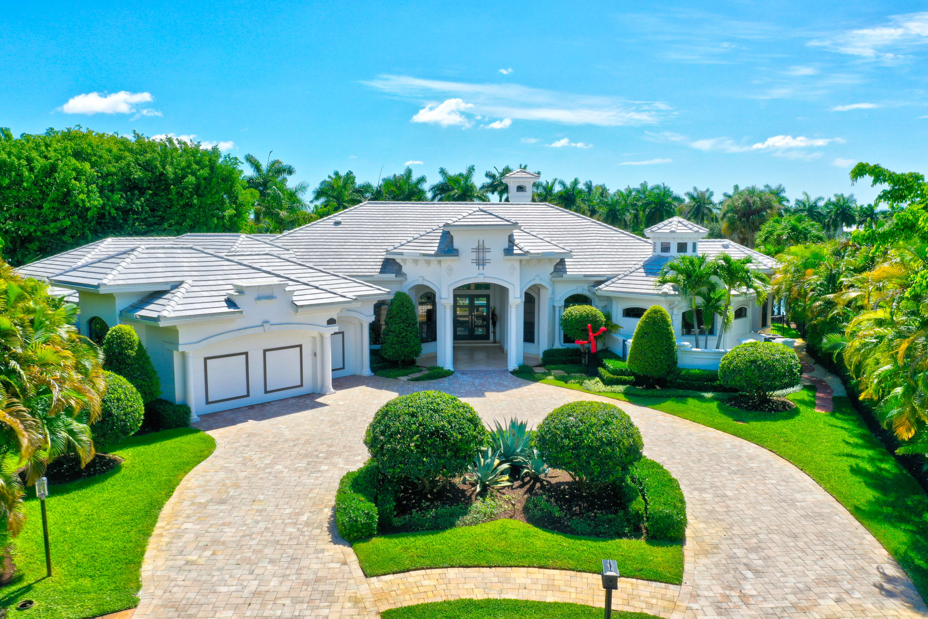 This Mediterranean style home is an architectural delight. Situated on a very private, pie-shaped lot at the end of a cul-de-sac. The expansive resort-stye pool area offers scenic views onto the lake, nestled between luscious palms trees with plenty of green space. 4 bedroom/2 office/6.5 bath, 2004 custom built home offers 5,520 sq. ft. ideally divided into separate wings; Master Bedroom wing, features an expansive master suite with his / her baths, overgenerous closets and intimate retreat off the bedroom; a great space for an office or private dressing room. The Guest wing offers 3 spacious ensuite bedrooms, all with beautifully appointed baths and walk-in closets w/ custom shelving. 3 of the homes bedrooms enjoy their own private patio courtyards, accessed by French doors (Roof 2020) The Wings of the home are connected by a grand formal great room, formal dining room, office, family and morning room, large bright kitchen, butlers pantry, separate bar bridging the dining room with the kitchen, elegant powder room and full cabana bath with shower. Following the spacious laundry room is the 2.5 car garage, with cabinetry and plenty of storage space.
The open and bright main living area enjoys floor to ceiling windows providing breathtaking views and tons of natural light right as you walk in, 24" travertine flooring laid on the diagonal and a custom fireplace surround enhances the space as you enter into the home. Off to the side of the main living area is a custom built-in office with warm wood floors and a formal dining room, while the Sonos sound system is powered through the whole home. Spacious laundry room leads into the 2.5 car garage, with cabinetry and plenty of storage space.