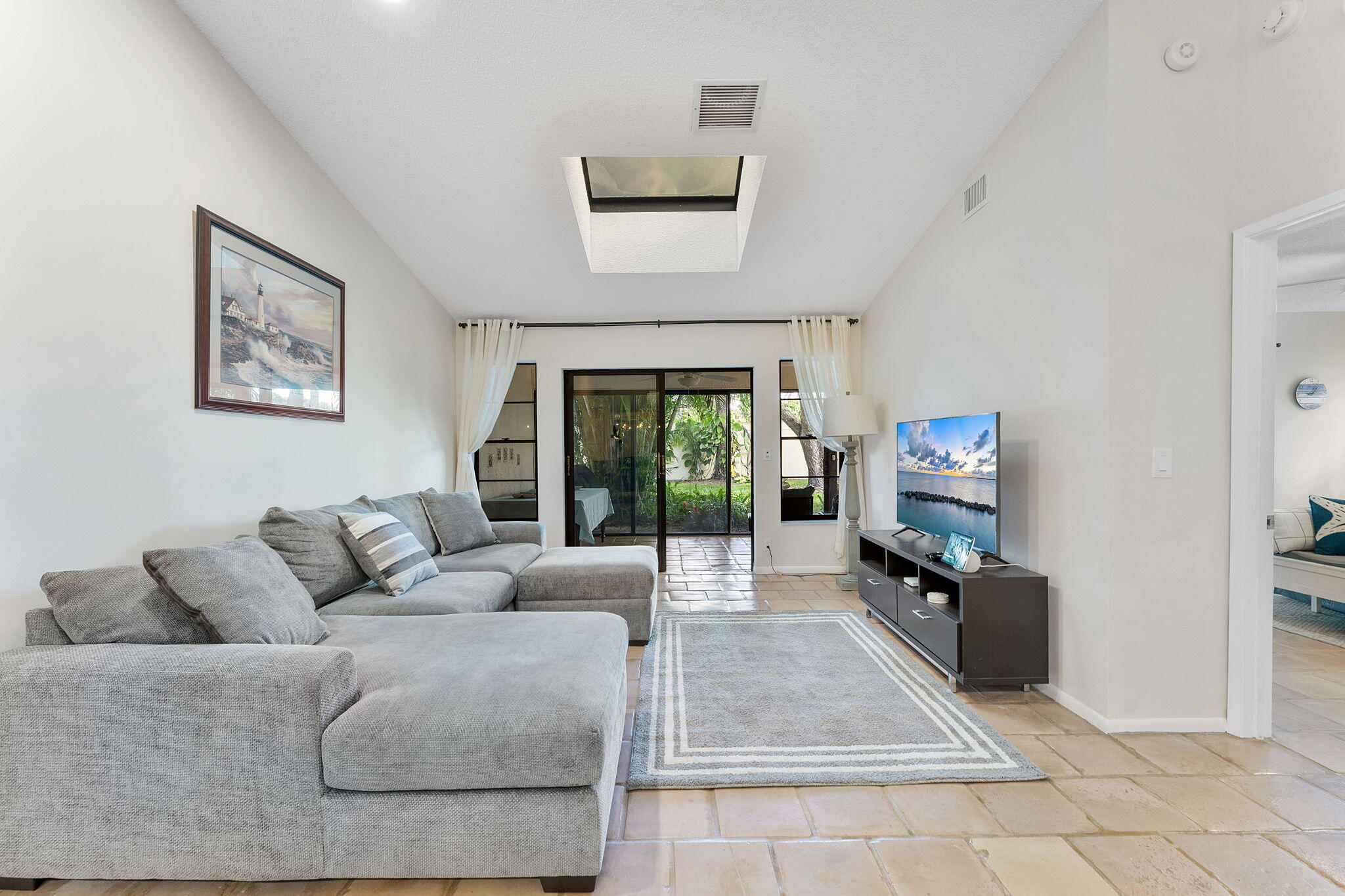 This beautiful villa offers the perfect blend of coastal comfort and modern convenience, featuring a signature red-tile roof and a spacious one-car garage. Inside, the bright, open-concept living area boasts soaring vaulted ceilings, a skylight for abundant natural light, and elegant neutral tile flooring that flows throughout the home. The dining space and breakfast bar overlook a sleek, updated kitchen, while the generous primary suite offers direct access to the patio. Transition seamlessly into the expansive enclosed sunroom, which offers a serene view of the lush tropical landscaping. Complete with a dedicated laundry room and meticulously updated bathrooms, this move-in-ready gem is designed for effortless Florida living.