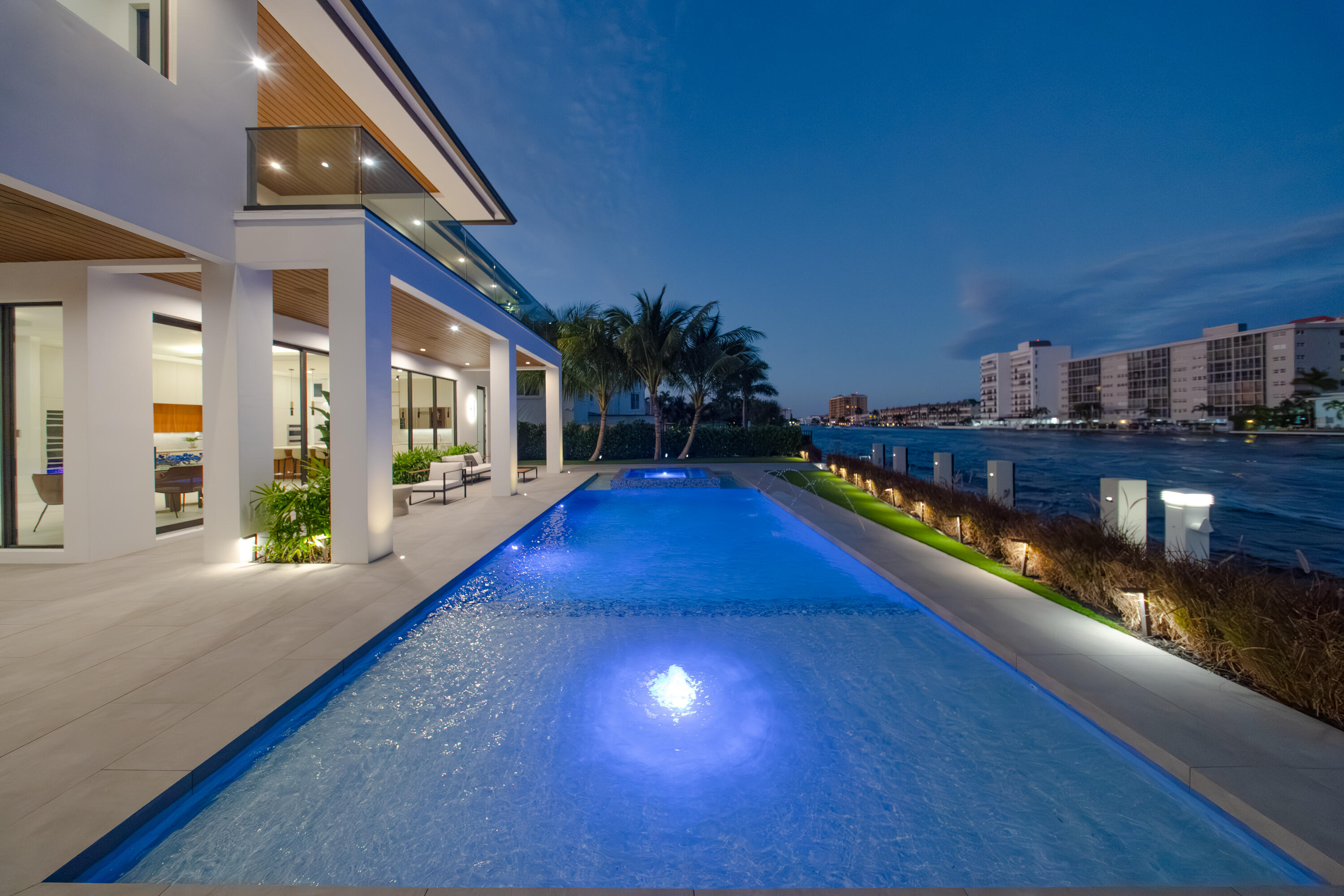 A modern masterpiece sited on the main intracoastal offering unrestricted saltwater and seamless direct ocean access. This estate seamlessly blends sleek architectural design, luxurious amenities, and cutting-edge technology to offer an exceptional South Florida lifestyle. Nestled minutes from Hillsboro and Boca Inlets, this waterfront home is ideal for yachting enthusiasts with its 91-foot yacht dock complete with bumpers, cleats, Shore Power Pedestal, and water supply, all secured by robust concrete pilings and evening lighting. The home's custom architectural design is captivating, combining tropical landscaping with expansive 10-foot PGT impact glass doors that welcome natural light while connecting indoor and outdoor spaces. An entertainer's paradise, the exterior offers a spacious loggia with a summer kitchen, a gas-powered concrete fire bowl for ambiance, and a saltwater pool and spa with sun shelves, LED bubblers, a spillway, and powerful jets all controlled by the smart home automation system. The second-story covered balcony is thoughtfully equipped with cable railings, water spigots, and a smart home interface. Inside, 12-foot ceilings enhance the sense of grandeur, while panoramic water views set the tone for the open floor plan. Sophisticated finishes like European oak engineered hardwood and expansive 48x48 porcelain tiles grace the living spaces, anchored by a water vapor LED-lit fireplace in the formal living area. A custom LED-lit staircase with glass railings and wood capping serves as a stunning architectural feature in the bright, welcoming foyer. The gourmet kitchen is a culinary dream, complete with leathered Taj Mahal quartz countertops, and high-end Monogram and Bosch appliances, including dual built-in refrigerators, a Bosch espresso machine, and a Thermador wine fridge. A jumbo-sized island provides ample seating and prep space, while a central vacuum with toe-kick features keeps the kitchen spotless. The butler's pantry, trimless recessed lighting, and dedicated office space with glass doors and custom cabinetry add both functionality and style. The primary suite is a sanctuary, boasting waterway views from a private terrace, a custom breakfast bar, his-and-her vanities, an elegant makeup vanity, and expansive walk-in closets. The oversized shower, designed as a spa-like retreat, includes dual rain heads, body jets, and floating benches. A mother-in-law suite on the main floor offers privacy and comfort, with easy access to the pool, dock, and outdoor shower via a cabana bath. Equipped with advanced smart home and security systems, the property features a Ring doorbell, four CCTV cameras, motion-sensor flood lights, and comprehensive automation that controls lighting, climate, pool, and security. Energy-efficient features include Low-E glass, tankless water heaters, R-20 foam insulation, gas lines for essential appliances, and a generator-ready setup for added reliability. A two-zone 17 SEER HVAC system ensures optimal temperature control, while a 600 AMP underground electrical service and Cat-6 wiring throughout the home keep it future-ready.  Adding convenience, dual laundry rooms, a mudroom with custom storage, and an oversized three-car garage with car lift compatibility, utility sink, central vacuum, and side-mounted motor provide ample functionality. Thoughtfully designed down to the last detail, a private waterfront oasis offering elegance and cutting-edge technology, for a truly luxurious lifestyle.