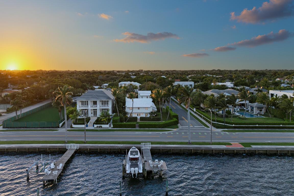 Set on a corner lot along South Flagler Drive, this West Palm Beach residence offers 70 feet of Intracoastal frontage on a 12,197+/- square foot lot with a private dock and pool. A thoughtfully integrated addition and a newly constructed guest house with a two-car garage and apartment above further enhance the property's scale, flexibility, and waterfront lifestyle.  The residence encompasses approximately 5,712+/- total square feet with five bedrooms, four full bathrooms, and two half bathrooms. From the moment of entry, the home is defined by natural light and sweeping water views.  The living room captures the Intracoastal setting, with windows framing the water, and serves as a central gathering space for everyday living. Just beyond, a sunroom with a built-in bar overlooks the pool and loggia and is outfitted with two under-counter refrigerators and an ice maker, well suited for relaxed gatherings and evening occasions. The dining room, featuring herringbone wood floors and a bay window, is surrounded by water views and opens directly to the kitchen, allowing for a natural flow between spaces.  The eat-in kitchen is both refined and highly functional, appointed with custom Poggenpohl cabinetry, an internationally recognized German brand known for its precision engineering, clean lines, and exceptional craftsmanship. Dacor appliances include an induction cooktop, large refrigerator and freezer, and two dishwashers, complemented by extensive integrated storage and a dedicated coffee bar. A substantial island, with additional storage, anchors the space and opens to the family room, creating a comfortable layout for daily living.  The family room overlooks the pool and terrace, with sliding glass doors enhancing the connection to the outdoors. Also on this level are a full laundry room and a well-appointed guest suite, which features a walk-in closet and an en suite bath with dual sinks, a separate tub and shower, and a private water closet.  The upper level is dedicated to the primary suite and additional guest accommodations. The primary bedroom enjoys commanding water views and includes a spacious walk-in closet and a serene bathroom with a separate tub and shower. Two additional guest bedrooms are also located upstairs, each with its own closet and sharing a thoughtfully designed bathroom with dual sinks and a walk-in shower.  The guest house, located above the air-conditioned two-car garage, offers exceptional flexibility for extended stays. The apartment includes a living room with a full kitchen featuring an induction cooktop, oven, refrigerator and freezer, and a Bosch dishwasher. The guest bedroom includes closets, an en suite bath, and a washer and dryer.  Outdoor living is a defining element of the property. The pool area is anchored by a covered loggia and coquina terrace, connected by a long covered breezeway. A generous gathering area on the western side of the pool includes a built-in grill, cabana bath, and outdoor shower, creating a private setting suited for both relaxation and hosting.  The private dock is equipped with a 24,000 lb boat lift, electric, and water, providing convenient access to the Intracoastal and complementing the home's waterfront lifestyle.  A rare opportunity to own a thoughtfully designed Intracoastal residence with dockage, guest accommodations, and refined interiors, ideally positioned along one of West Palm Beach's most desirable waterfront corridors.