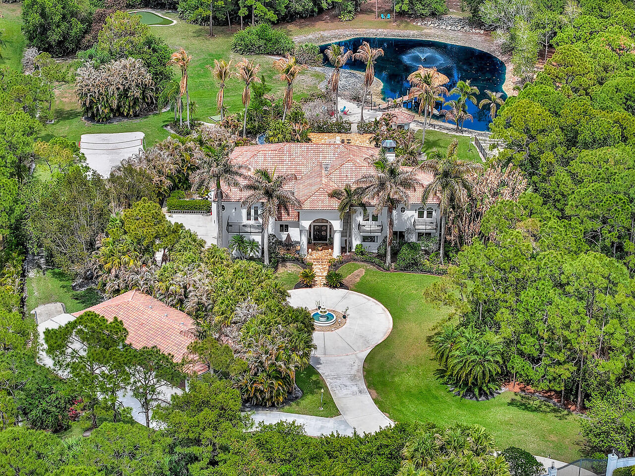 Serene. Secluded. Exclusive.  Welcome to 2584 SE Ranch Acres Circle in Jupiter—a private estate designed for those who appreciate space, recreation, and refined living.  Set across more than five acres of beautifully landscaped grounds, this nearly 10,000 total square foot estate offers an extraordinary collection of amenities rarely found in a private residence.  Outdoor living is the centerpiece of the property. The grounds feature a sandy beach volleyball court, a private par-3 golf hole with driving range, and a scenic lakefront retreat complete with a beach, 50-foot dock with an open-air living room beneath a newly constructed tiki hut. A walking trail encircles the entire fenced estate, creating a peaceful path through the property. (See supplemental remarks) For those who appreciate a connection to nature, the estate also includes a custom chicken habitat with a 600-square-foot designer coop.   The swimming pool, measuring **50 x 30 feet—nearly twice the size of a standard residential pool—**features a dramatic waterfall and expansive entertaining areas designed for gatherings both intimate and grand.  Inside the home, a high-end renovation has been completed, bringing modern luxury to every detail. The kitchen showcases Cristallo stone countertops with under-lit surfaces, Sub-Zero appliances, and a striking beamed ceiling. The primary bath and three additional bathrooms have been completely reimagined, blending contemporary elegance with spa-like comfort. Custom impact windows and doors are currently being made, enhancing both beauty and resilience.  Additional lifestyle features include a private media room, a separate in-law suite with full bath (currently used as a fitness studio), and a detached six-car climate-controlled "man cave" garage. Including the main house garages, the property offers 10 total garage bays—a rare amenity ideal for collectors and enthusiasts. This is Ranch Colony living at its most exceptional—private, sportive, and unmistakably luxurious.