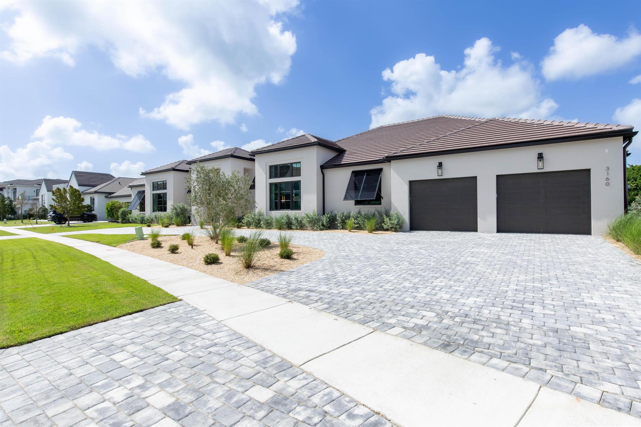 This magnificent new construction estate is situated on a double lot in the new highly coveted neighborhood of Blue Cypress within the Palm Beach Polo Club. The expansive luxury home features 4 bedrooms, 5 full and 1 half baths, 2-car garage, and an eye-catching pool and spa. Showcasing an elevated contemporary style from the masterful designers at Soco Interiors, this home incorporates tranquil woods and neutrals accented with bold contrasting finishes, creating sophisticated and comfortable spaces. The courtyard-style floor plan presents an ultra private setting for the lavish primary suite in the east wing, featuring his and her walk-in closets, a sitting area and a private patio. Adjacent to the primary suite is a large study with a storage room/possible 5th bedroom, and a full cabana bathroom. The west wing of the home hosts the open concept chef's kitchen, great room with a fireplace, and a formal dining area with a stunning glass enclosed walk-in wine cellar. There are 3 guest bedrooms, each with walk-in closets, full baths, and two have access onto the patio. Stepping outside, the stunning courtyard pool area includes a large covered patio with a summer kitchen, lounging area, and a sleek black tiled pool and spa.