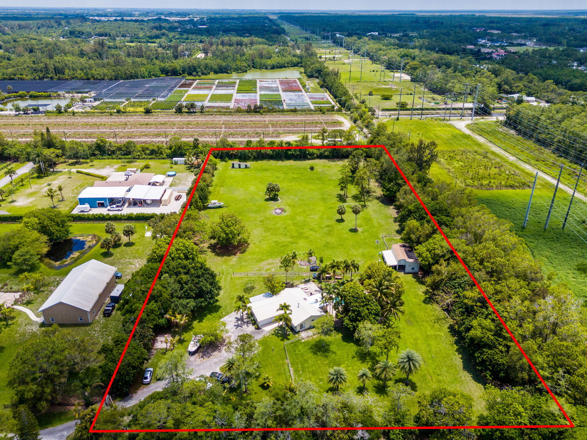 Located just minutes from Wellington's world-renowned horse show venues, this rare 4.66-acre equestrian property offers peaceful country living with expansive surroundings and endless potential. Comprised of two adjoining parcels being sold together and backing up to the prestigious Homeland equestrian community, the property features beautifully cleared land, mature trees, tropical landscaping, double canal frontage, and plenty of space to create or expand your ideal equestrian estate, all with no HOA. The home was designed to take advantage of the surrounding views and offers a spacious main living area with fireplace, pantry, walk-in closet, and primary suite, plus a separate guest wing with full kitchen, 2 bedrooms, 1 bathroom, and private living space.  Outside, enjoy a beautiful saltwater pool surrounded by scenic palms and bamboo privacy landscaping. Equestrian amenities include a 6-stall barn, additional 2.5-stall barn, water and electric to both barns, and expansive open grass areas. Additional features include an electric gate, metal roof (approx. 8 years), double-pane windows, panel shutters, and stainless steel appliances. A rare opportunity to own private acreage in a highly desirable Wellington area location close to equestrian venues, shopping and dining.   Metal Roof approximately 8 years old. both flat roofs (porch and sunroom) are brand new (May 2026), new wood porch (March 2026) BRAND NEW WELL (May 2026), New water softener (March 2026), AC(s) approximately 5 years and 12 years old Water heater approximately 5 years old