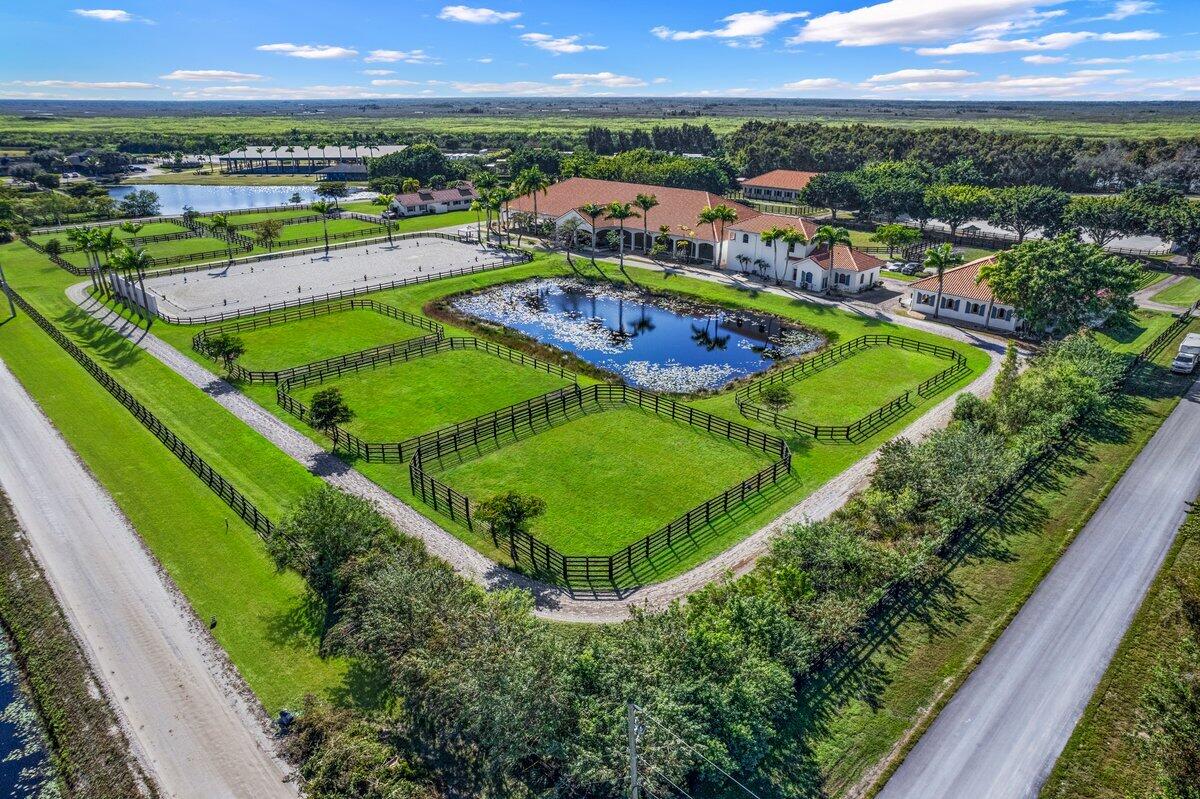 Enjoy the peaceful ambiance of this exceptional 20.72-acre professional Equine training facility with 4 barns totalling 41 stalls, 3 arenas (1 covered), 27 paddocks, a tree-shaded 6-horse Euro walker, Lunging ring, GGT exercise track, 3 apartments, and an owner's retreat, all nestled under the cool shade of mature, majestic Banyan and Royal Palm trees. Each of the 3 main show barns features a separate gated entry, fly spray systems, wash stalls, tack rooms, 1 staff apartment, barn bathrooms, feed rooms, privacy, functionality, and space for all equestrian disciplines. There are 37 main barn stalls, a 4-stall centre aisle pole barn with electricity, an attached tackroom, and two wash stalls. In addition, there are 8-In&Out stalls with generously sized paddocks, stall doors and electricity. Your horses will enjoy top-quality care with an on-site Equine Treatment/Exam room, an Aqua Treadmill, and two large farrier bays with automatic retractable awnings. The covered arena features an Ebb & Flow watering system, mirrors, lights and GGT footing. The 2-outdoor arenas are also mirrored and in private proximity to one another. The 3-bedroom owner's apartment is located on the second floor over two oversized garages and offers beautiful views of the farm. Owners will also have peace of mind with an excellent source of income-producing dry stalls, an 80 KW Kohler diesel generator, 4 RV hookups, a full farm water filtration system and plenty of space for horse trailers.