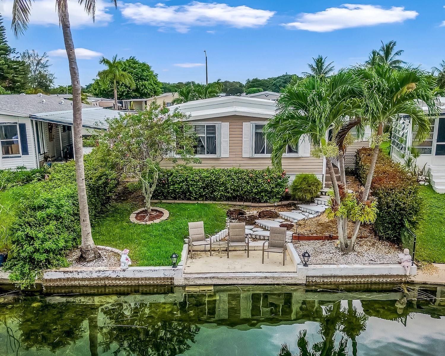 Discover this beautiful 2 bed, 2 bath home in the all-ages Estates of Fort Lauderdale, where you own the land. Key highlights include an updated kitchen with stainless steel appliances and custom cabinetry, newer flooring, and spacious bedroom with lots of natural light. Other features also include a large carport and accordion shutters throughout the home. With just over 1600 sq ft under air, this is one of the larger homes you'll find available in this community. Step outside to a backyard with a concrete dock just steps away, overlooking the lake creating a true tropical oasis. Come tour this gorgeous home today and make it your own slice of paradise.